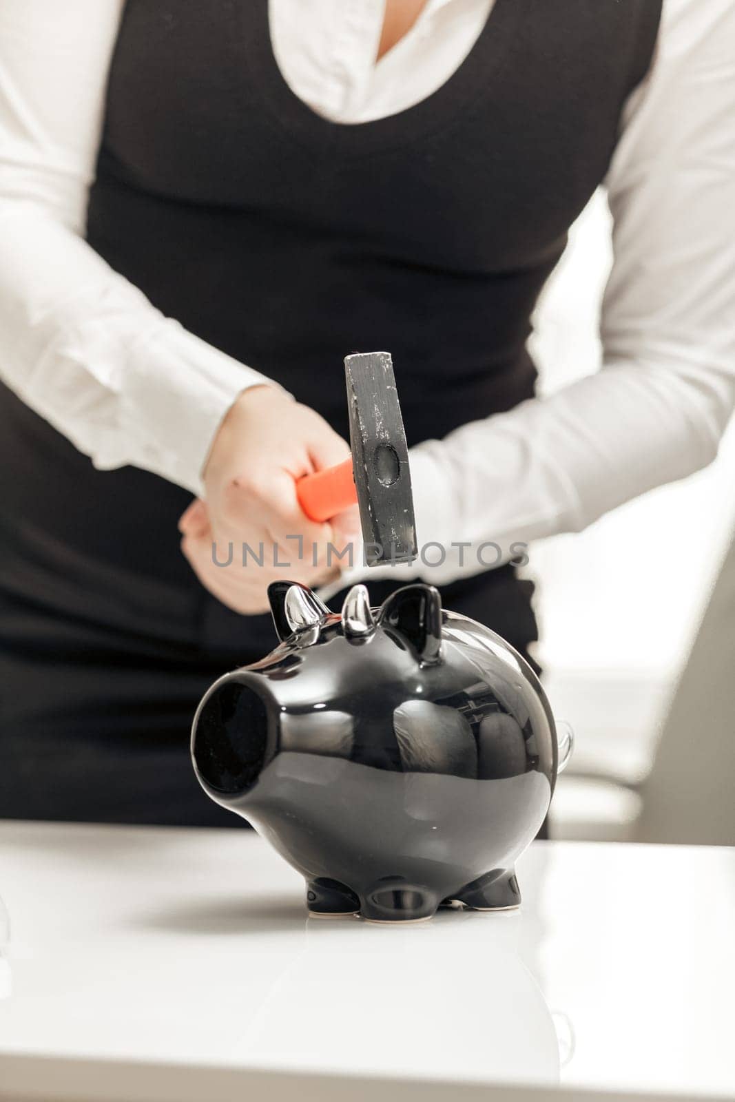 Young businesswoman hitting piggy bank with hammer