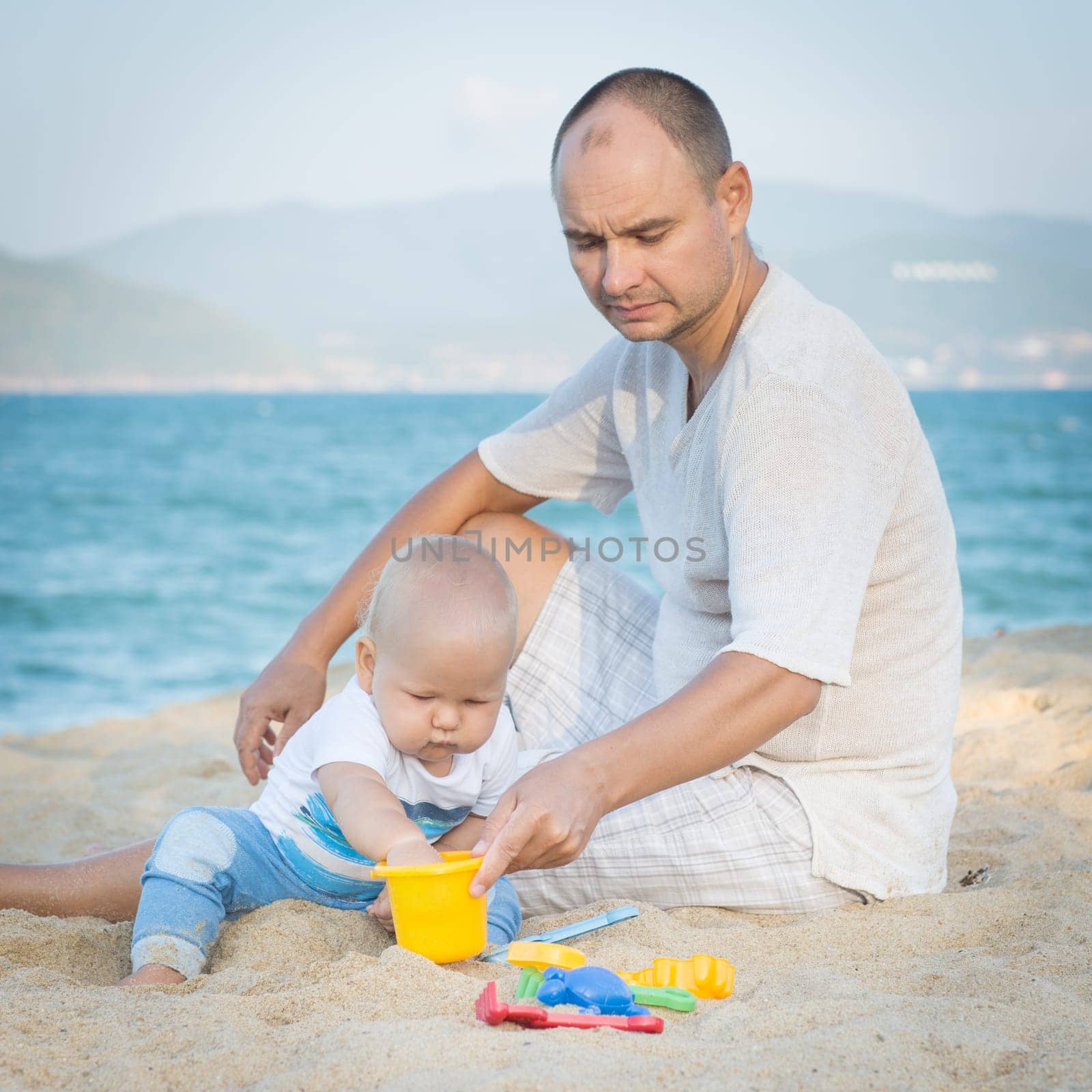 Father and baby are playing beach toys