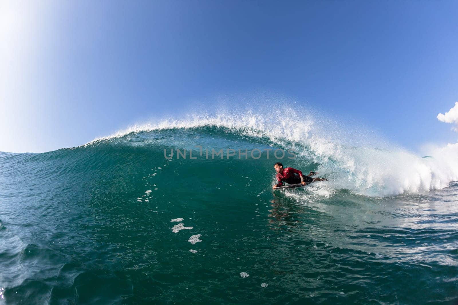 Surfing bodyboarder rides ocean blue wave crashing breaking onto reef beach shallows, a water photo perspective.