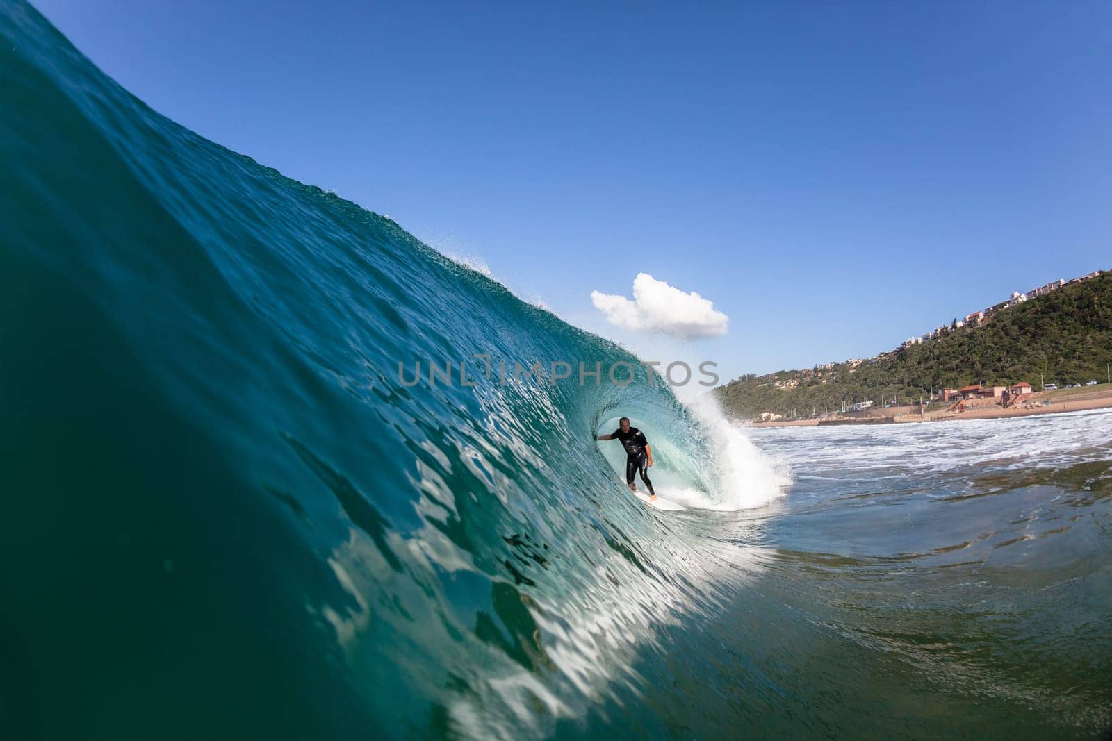 Surfer tube rides hollow blue wave wall upright round crashing breaking onto reef beach shallows, a water swimming photo perspective