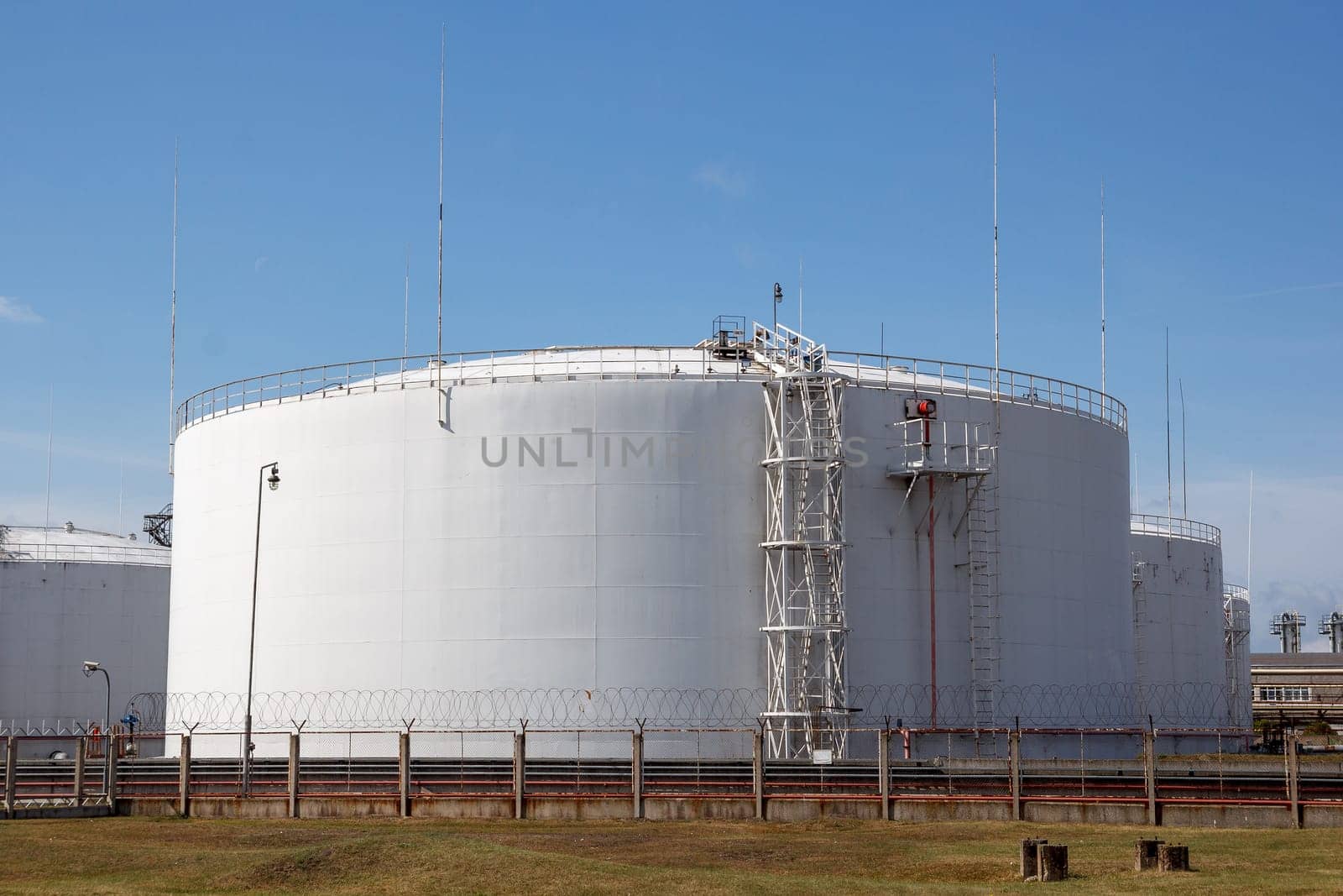 multiple white big oil storage tanks with a fence around them