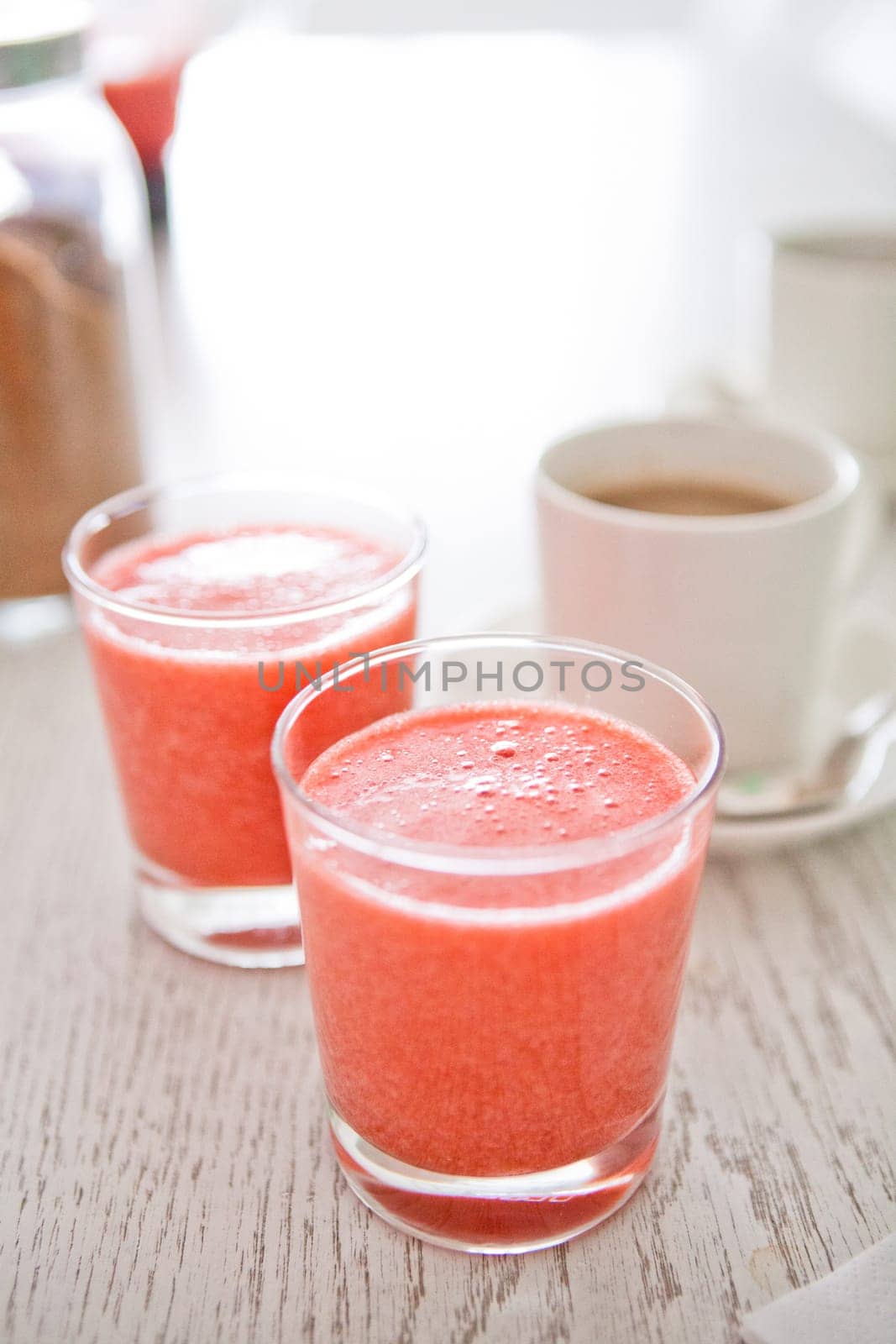 Closeup of two glasses of strawberry smoothies with cup of coffee in background