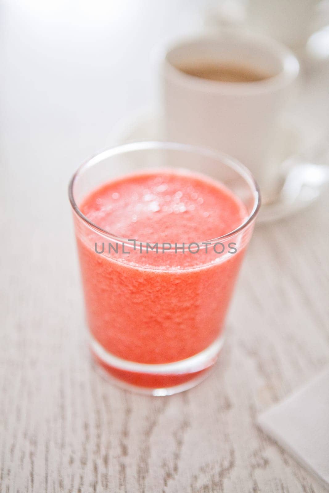 Closeup of strawberry smoothie in glass with cup of coffee in background