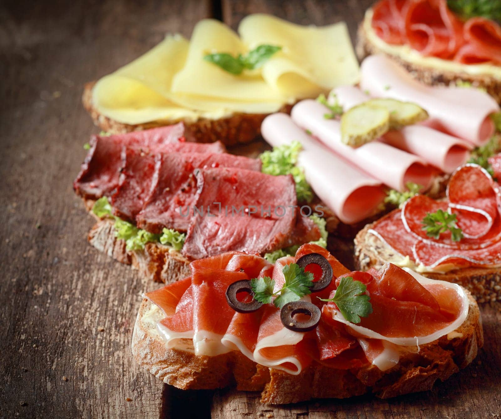 Selection of delicious open sandwiches topped with gouda cheese and assorted meats including roast beef, mortadella, ham and salami