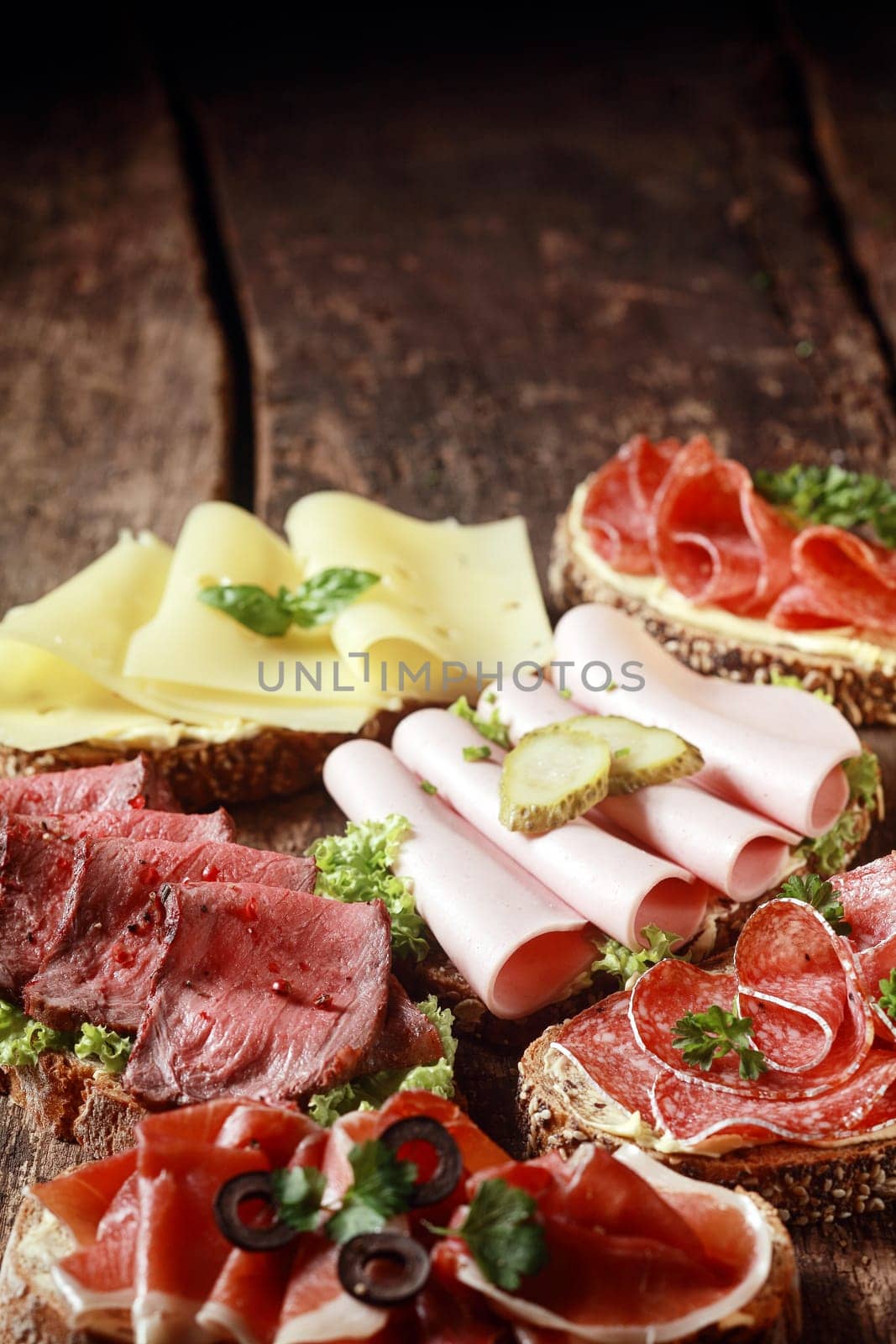 Assorted meat and cheese sandwiches with rare roast beef, mortadella, ham, gouda, salami, on rye and wholewheat bread on a rustic wooden table with copyspace