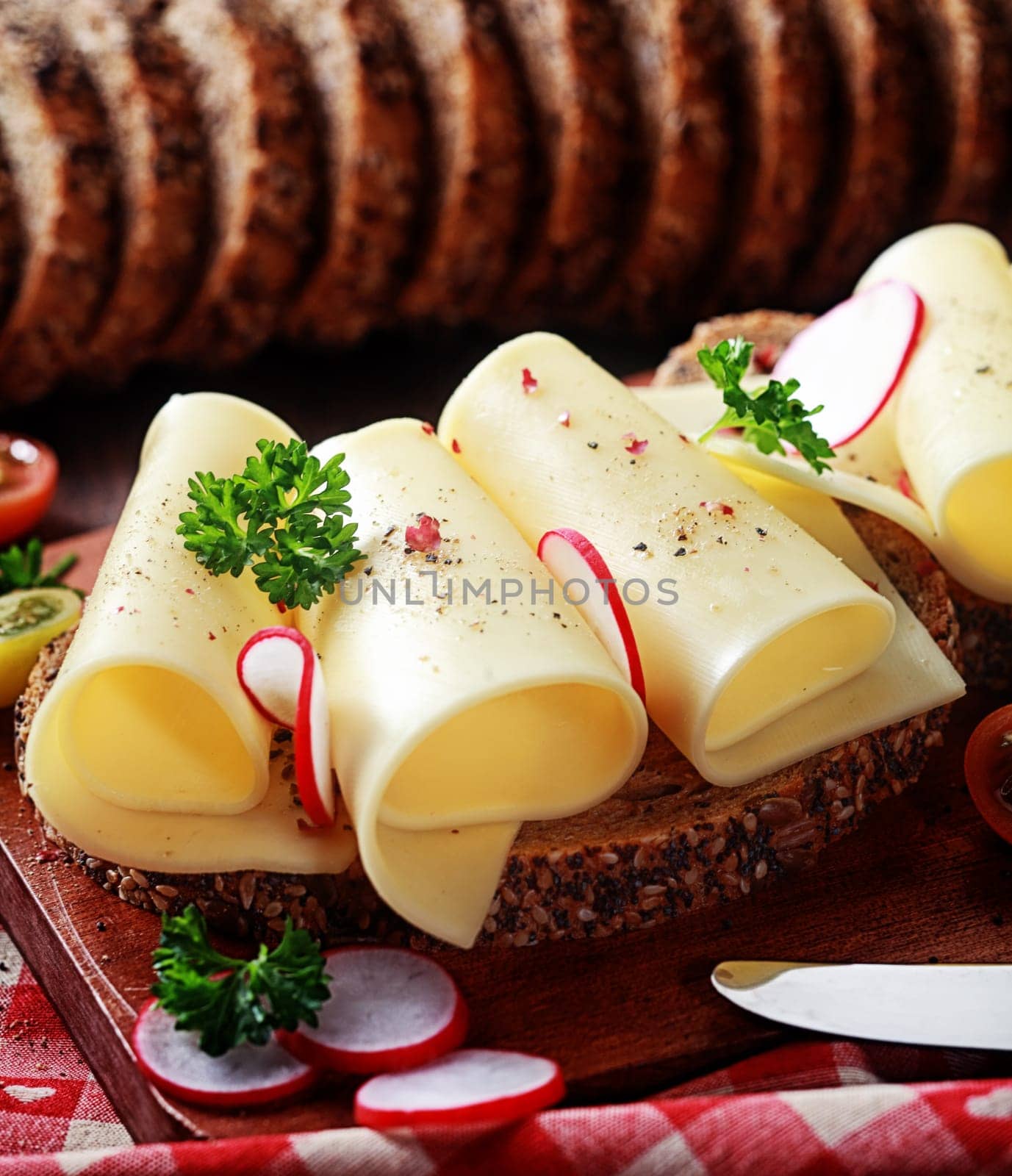 Fresh gouda cheese on wholewheat bread with thinly sliced radish and parsley seasoned with pepper and served on a wooden chopping board in a rustic kitchen