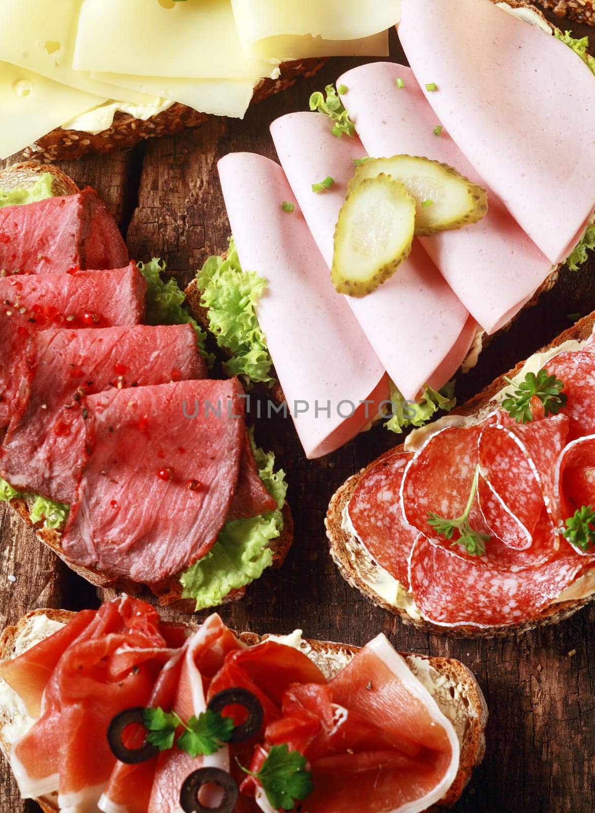 Array of tasty assorted open sandwiches on wholewheat and rye bread topped with gouda cheese, mortadella, roast beef, ham and salami