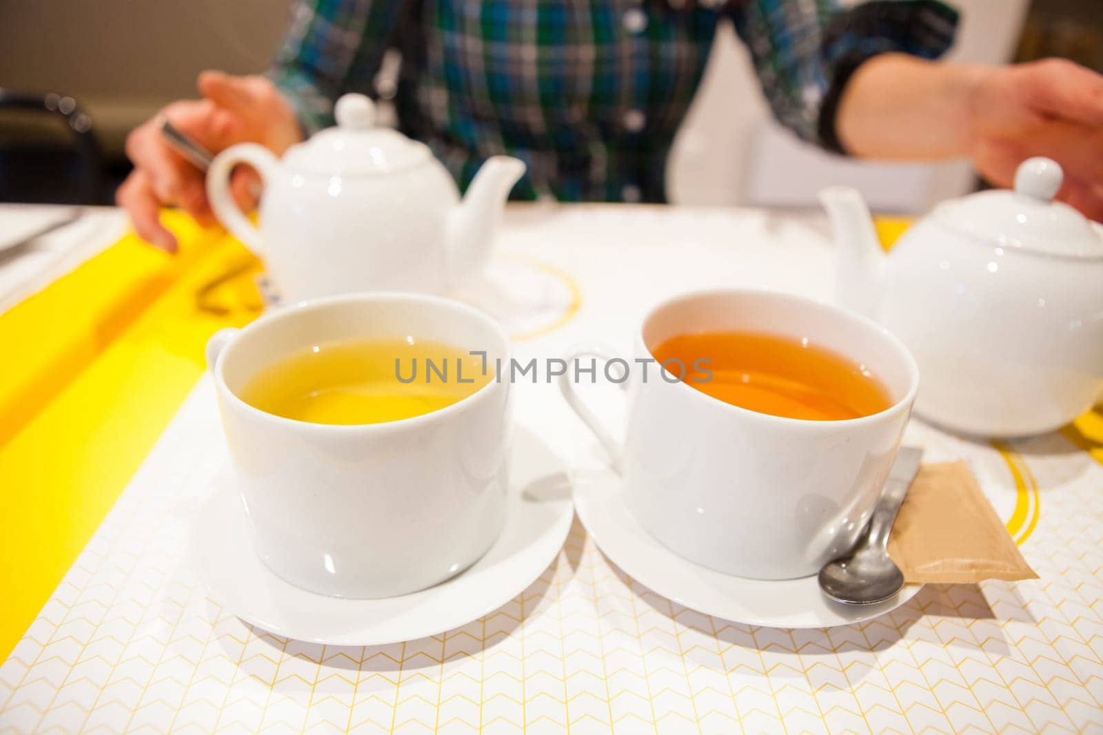 Closeup of two cups of herbal tea with tea pots and woman sitting in background