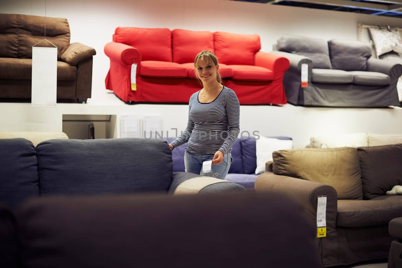 young hispanic woman shopping for furniture, sofa and home decor in store, looking at camera and smiling
