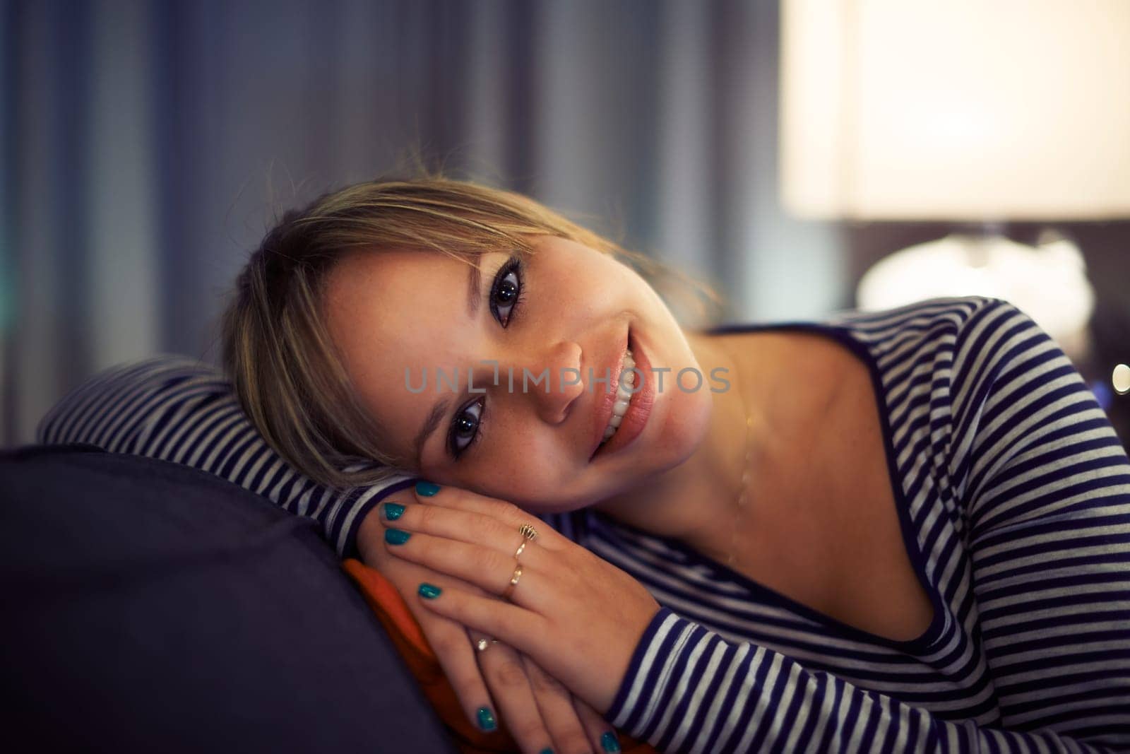 portrait of young blond hispanic girl relaxing on sofa at night and looking at camera smiling