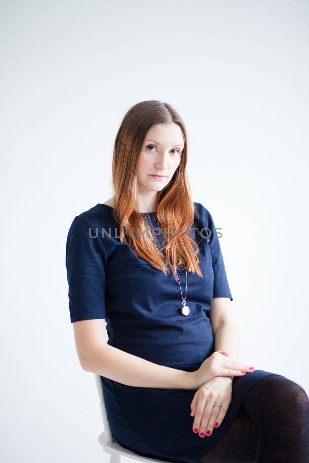 Studio portrait of thoughtful looking attractive woman wearing blue blouse and sitting in chair with hands resting on lap