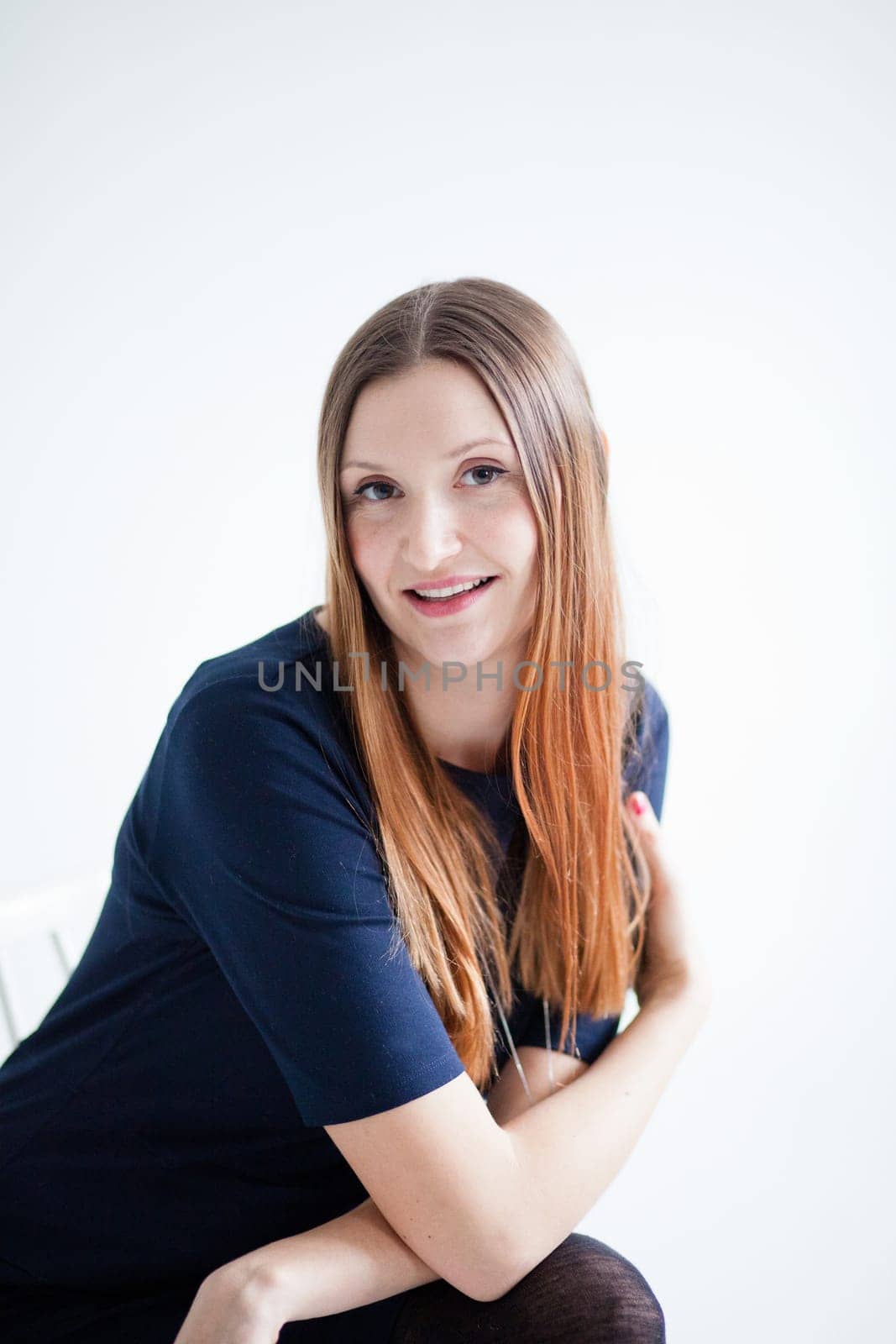 Studio portrait of happy smiling attractive woman wearing blue blouse and sitting with arms crossed
