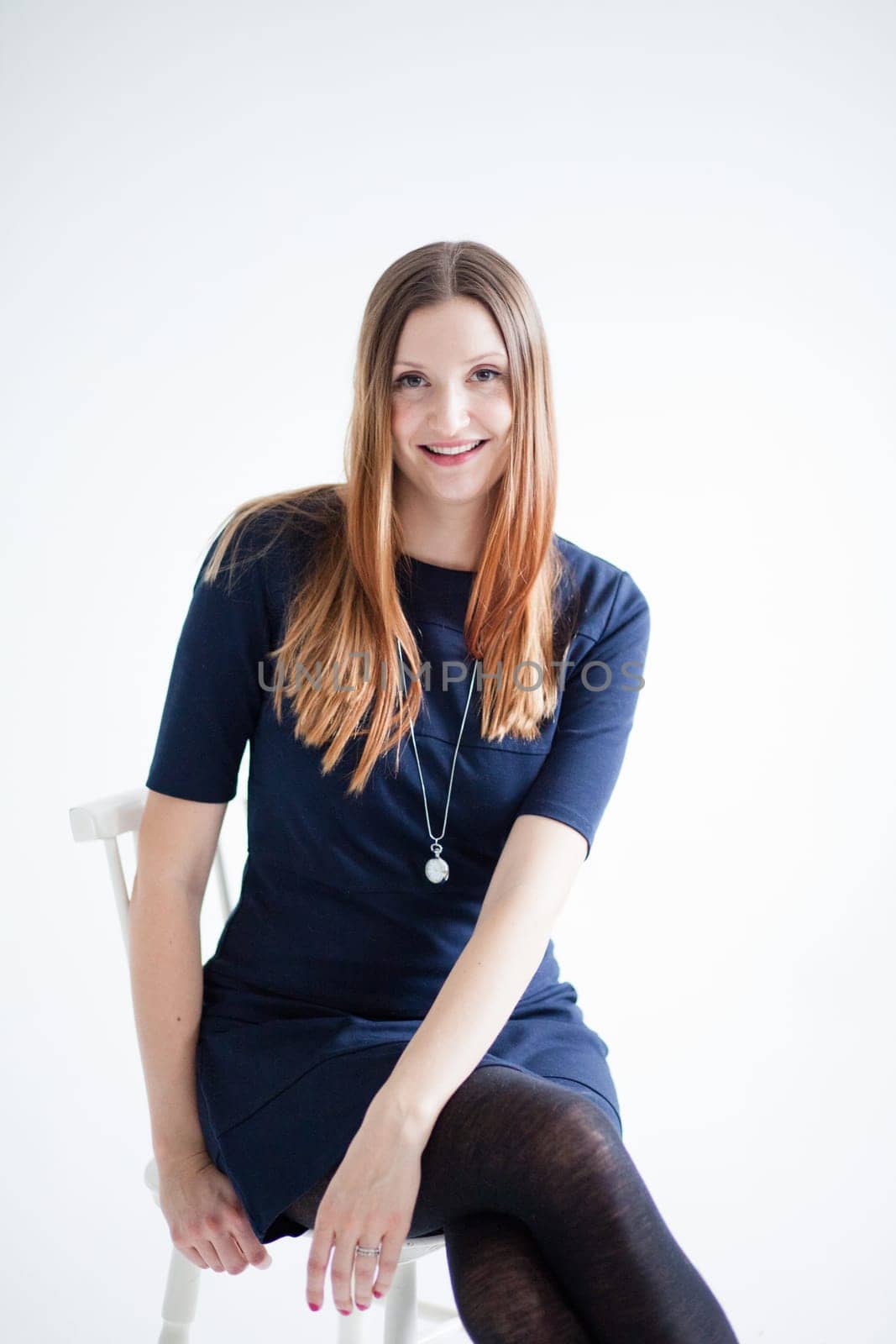 Studio portrait of happy smiling attractive woman wearing blue blouse and sitting in chair