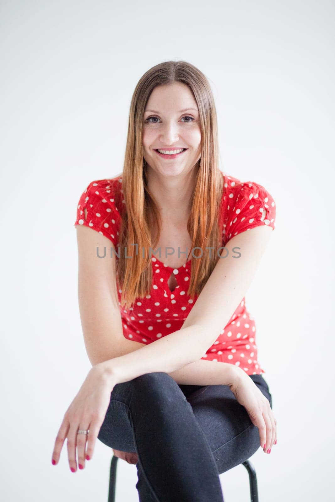 Studio portrait of happy smiling attractive woman sitting on stool and wearing red blouse