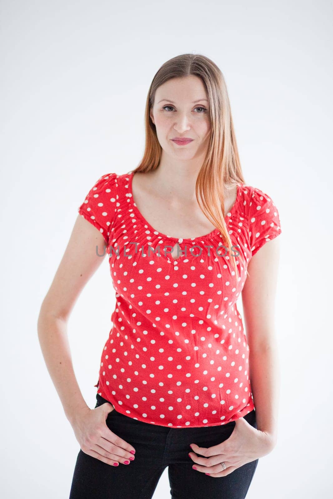 Studio portrait of attractive woman with happy smirk and wearing red blouse and standing with hands on hips
