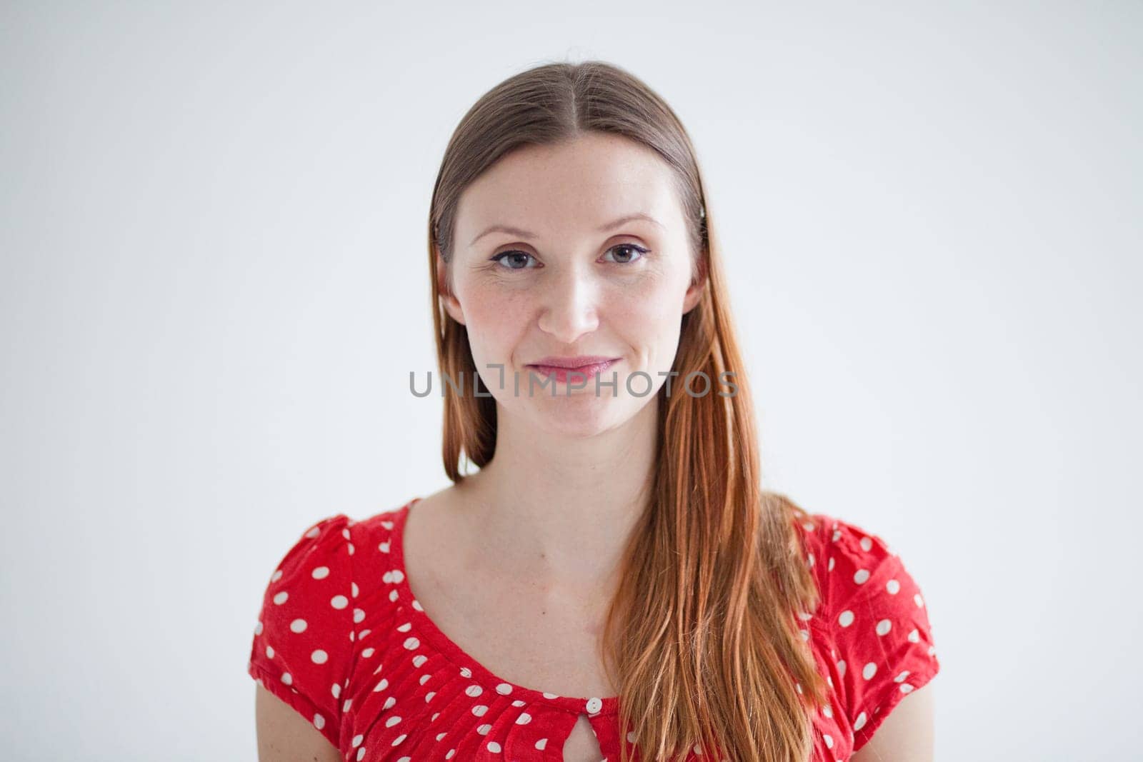 Studio portrait in landscape orientation of happy smiling attractive woman wearing spotty red blouse