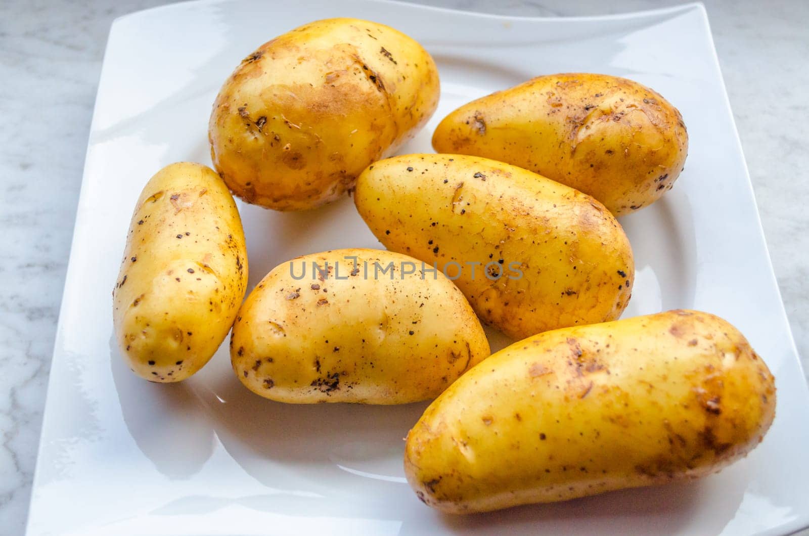 Six unpeeled raw potatoes on a white plate
