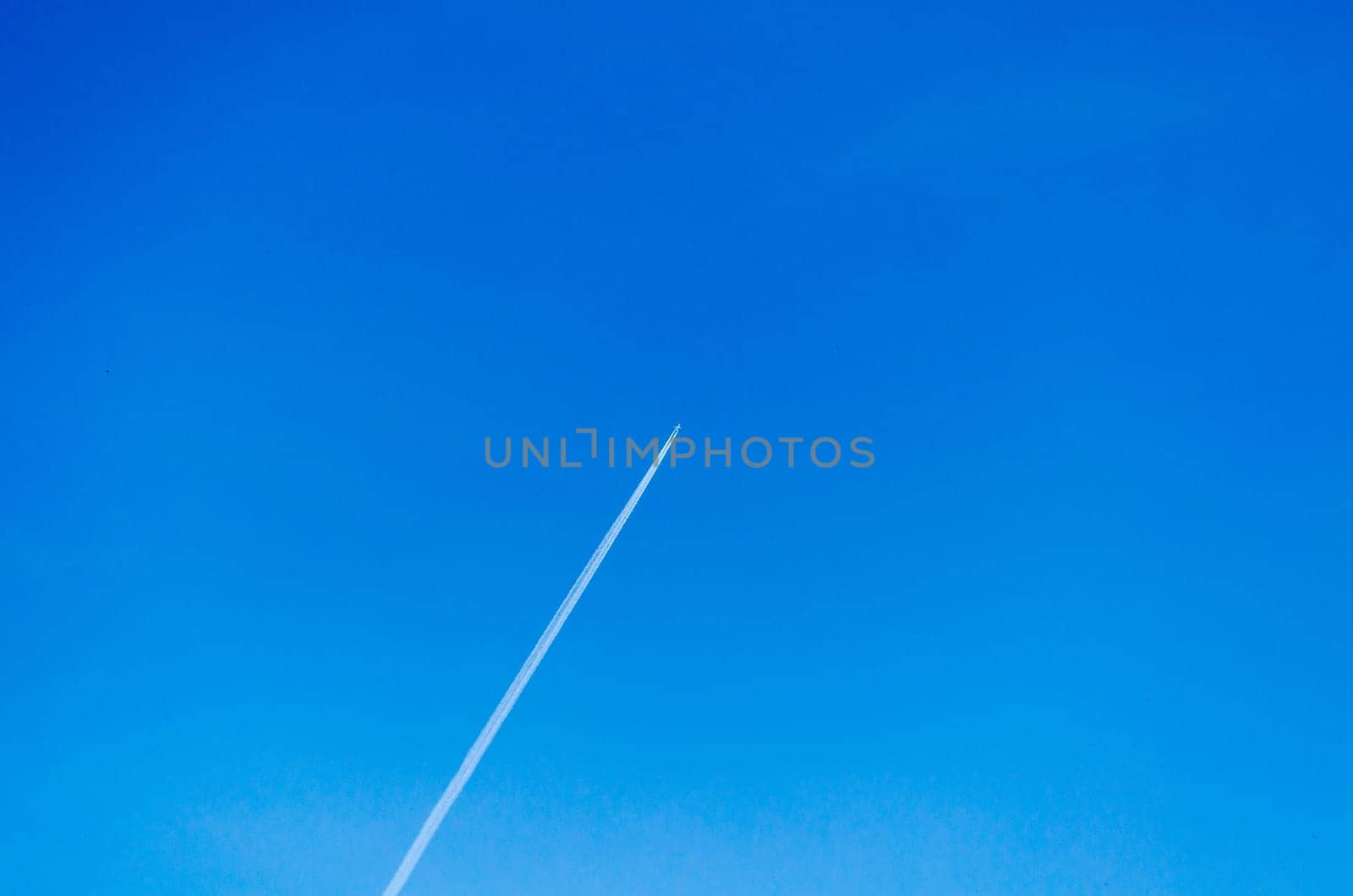 Plane leaves condensate strips in a cloudless sky.