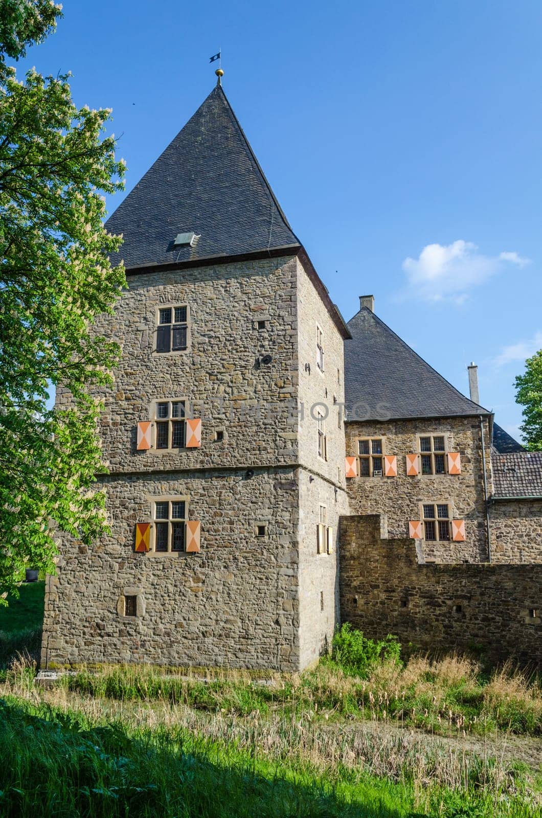 Old castle tower in front of blue sky and other historical parts of the building.