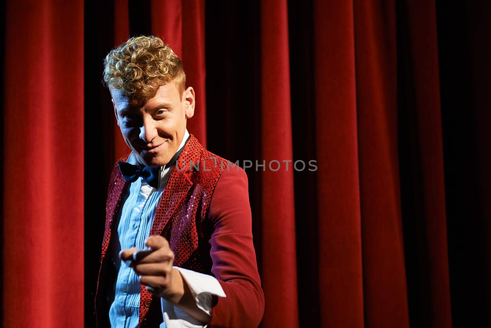 Arts and entertainment in theatre with funny man working as anchorman, standing against red curtains and pointing to camera