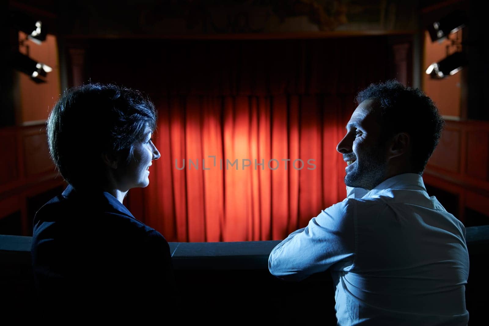 Arts and entertainment in theatre, with man and woman looking at stage with red curtains