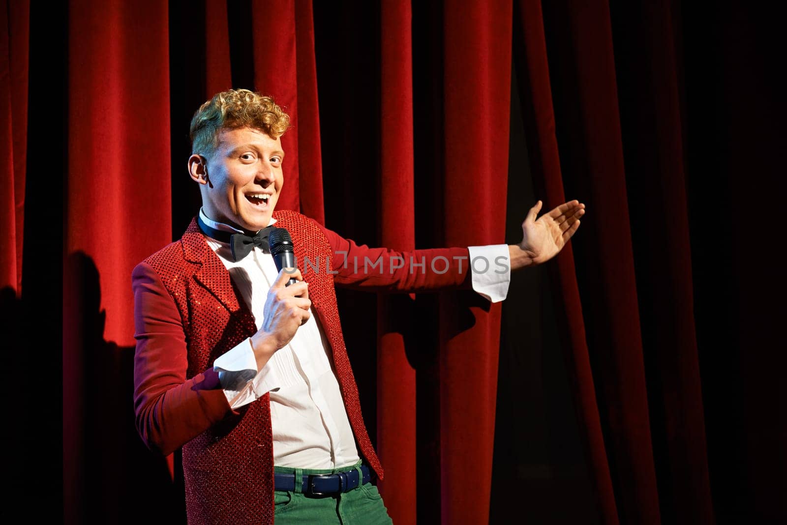 Arts and entertainment in theatre with funny man working as anchorman, standing against red curtains with microphone