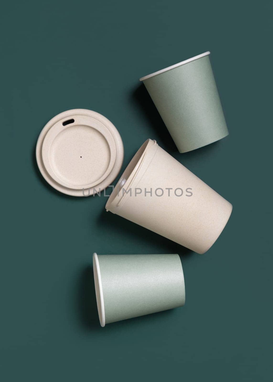 Disposable new light green paper cups and reusable bamboo coffee cup in a line a dark green top view, mockup with copy space. Empty coffee cups flat lay. No plastic and sustainable lifestyle concept
