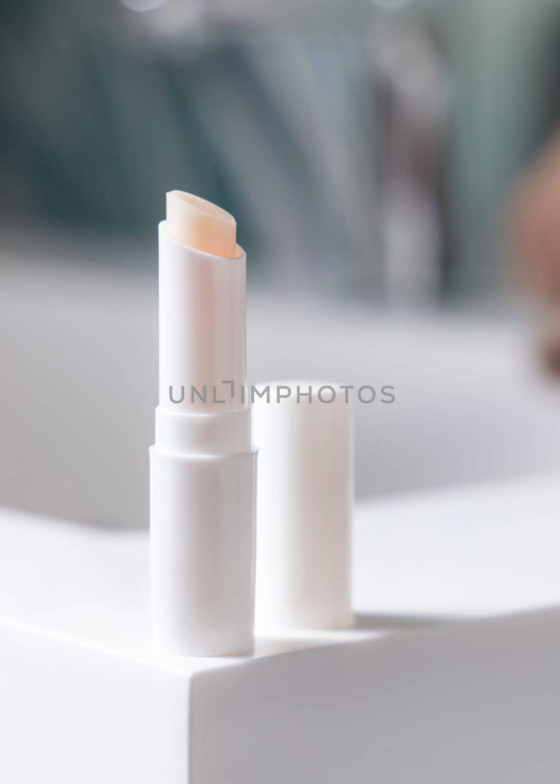 Opened white blank lip balm stick with a lid on basin in green tropical bathroom close up, packaging mockup with copy space. Lifestile scene with ubranded natural lipcare product