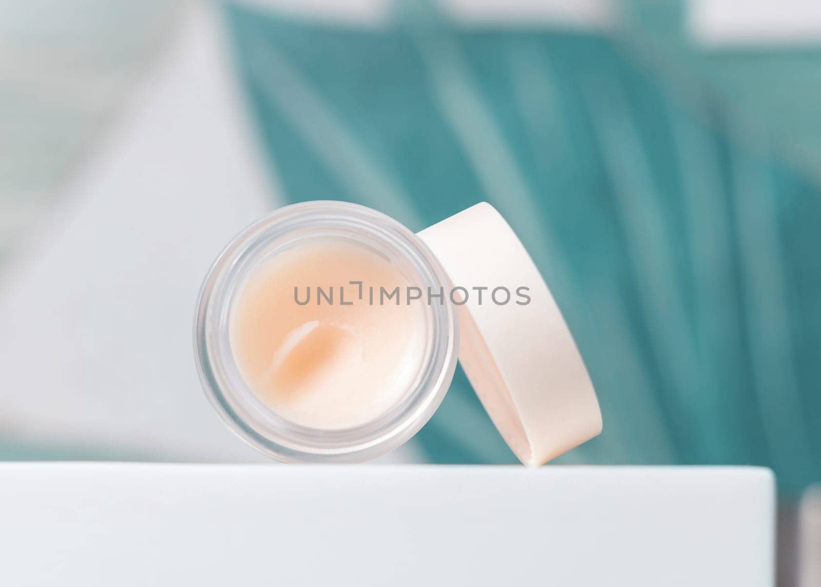 Opened white blank lip balm jar with a lid on washbasin with faucet in green tropical bathroom close up, packaging mockup. Lifestile scene with ubranded natural lipcare product