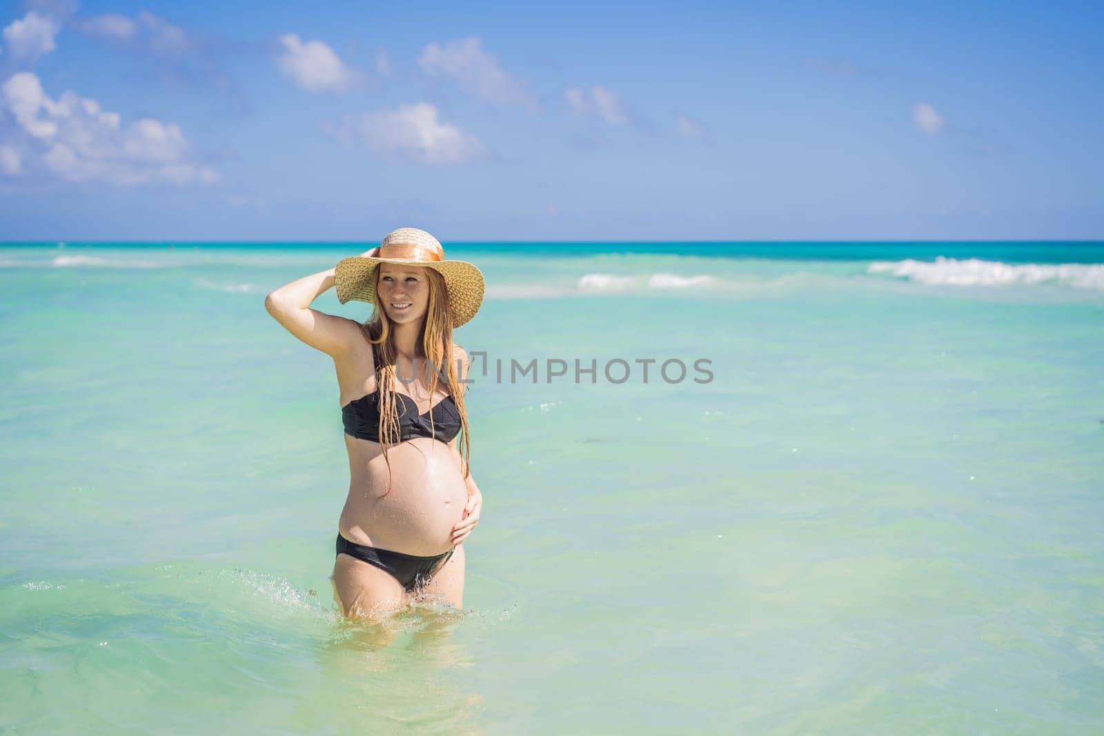 Radiant and expecting, a pregnant woman stands on a pristine snow-white tropical beach, celebrating the miracle of life against a backdrop of natural beauty.