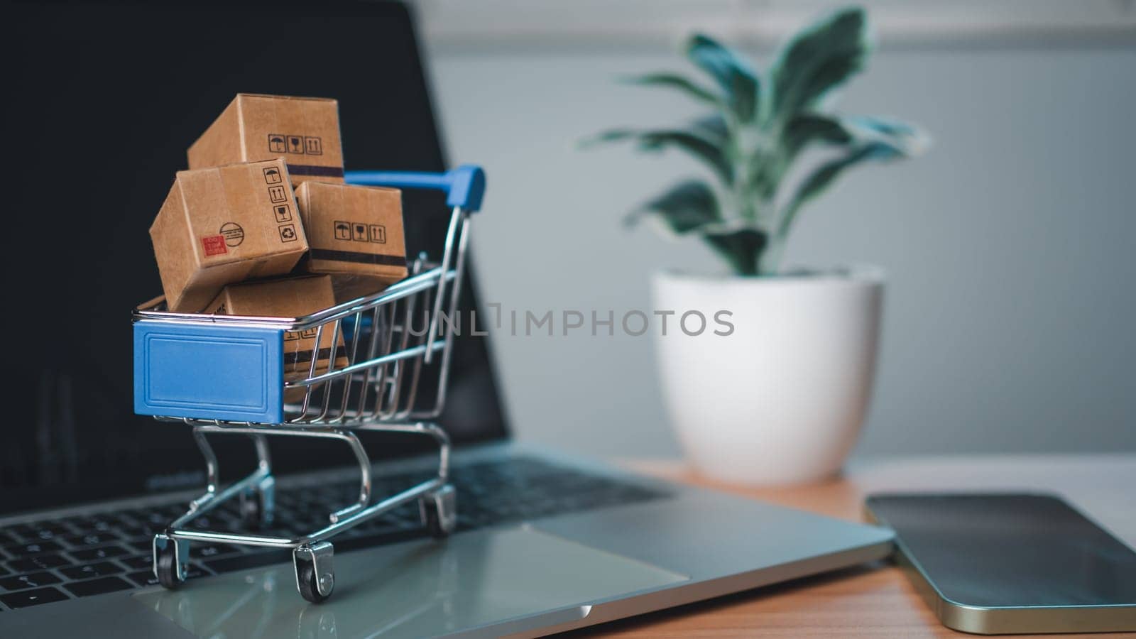 Shopping cart and product boxes placed on laptop computer represent online shopping concept, website, e-commerce, marketplace platform, technology, transportation, logistics and online payment concept.