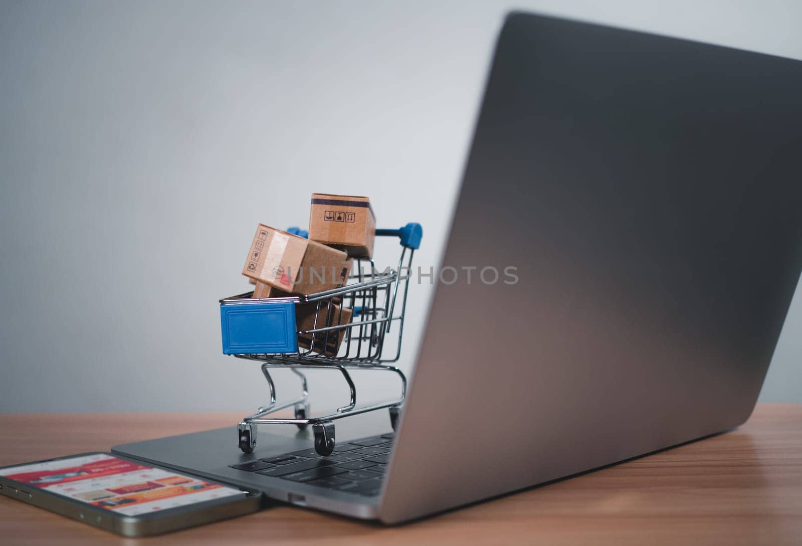 Shopping cart and product boxes placed on laptop computer represent online shopping concept, website, e-commerce, marketplace platform, technology, transportation, logistics and online payment concept. by Unimages2527