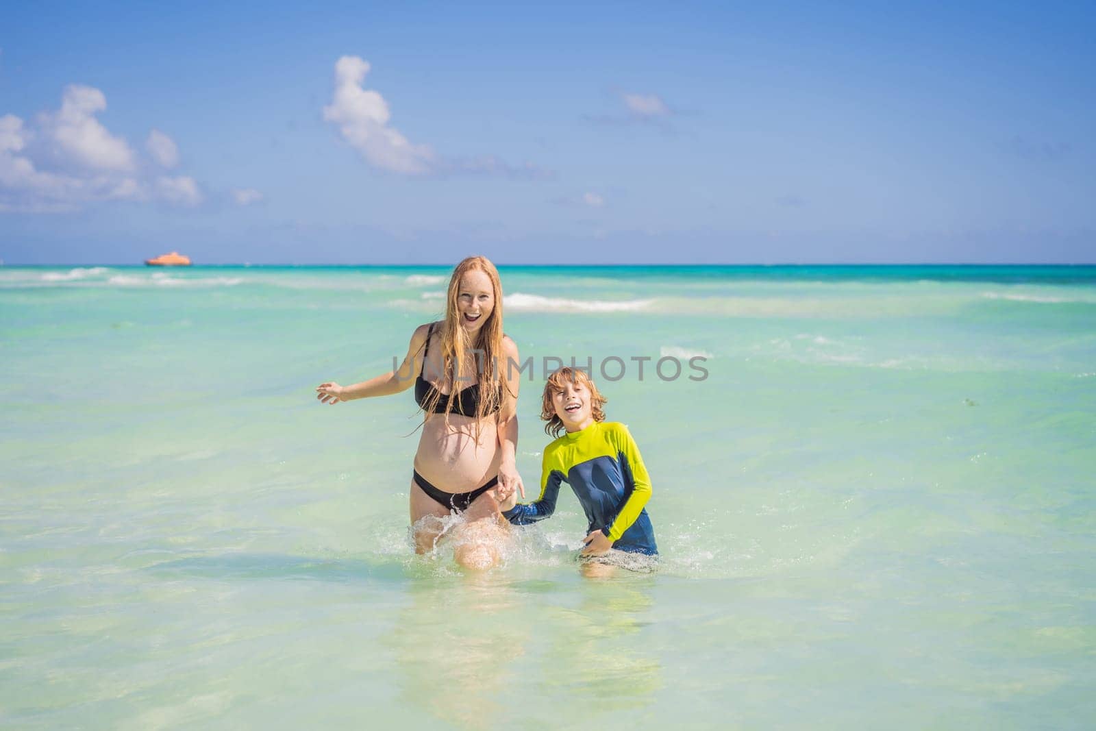 A radiant pregnant mother and her excited son share a tender moment on a serene, snow-white beach, celebrating family love amidst nature's beauty.