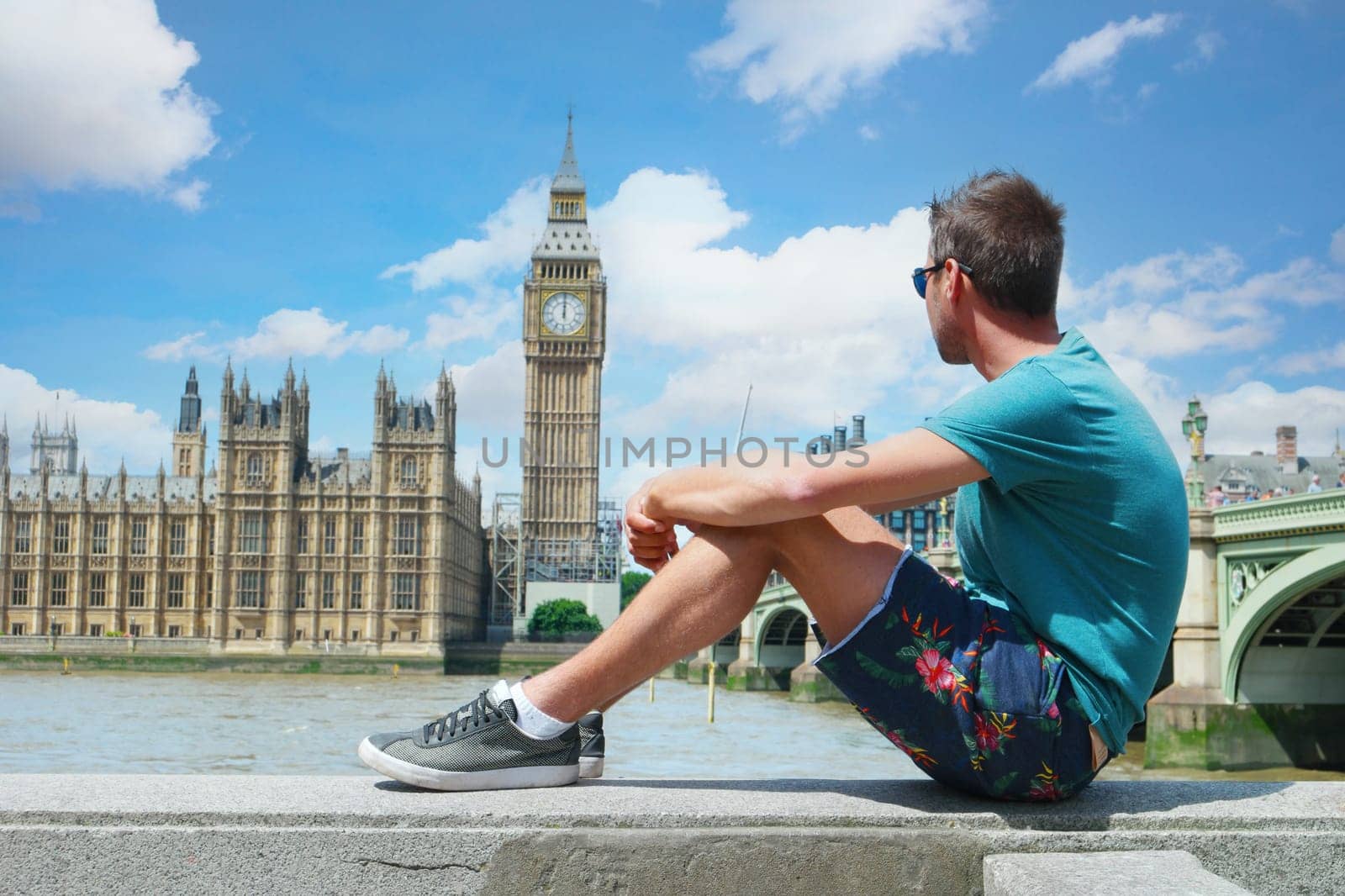 a young men tourist on a city trip in London looking at the Big Ben at Westminster Bridge by fokkebok