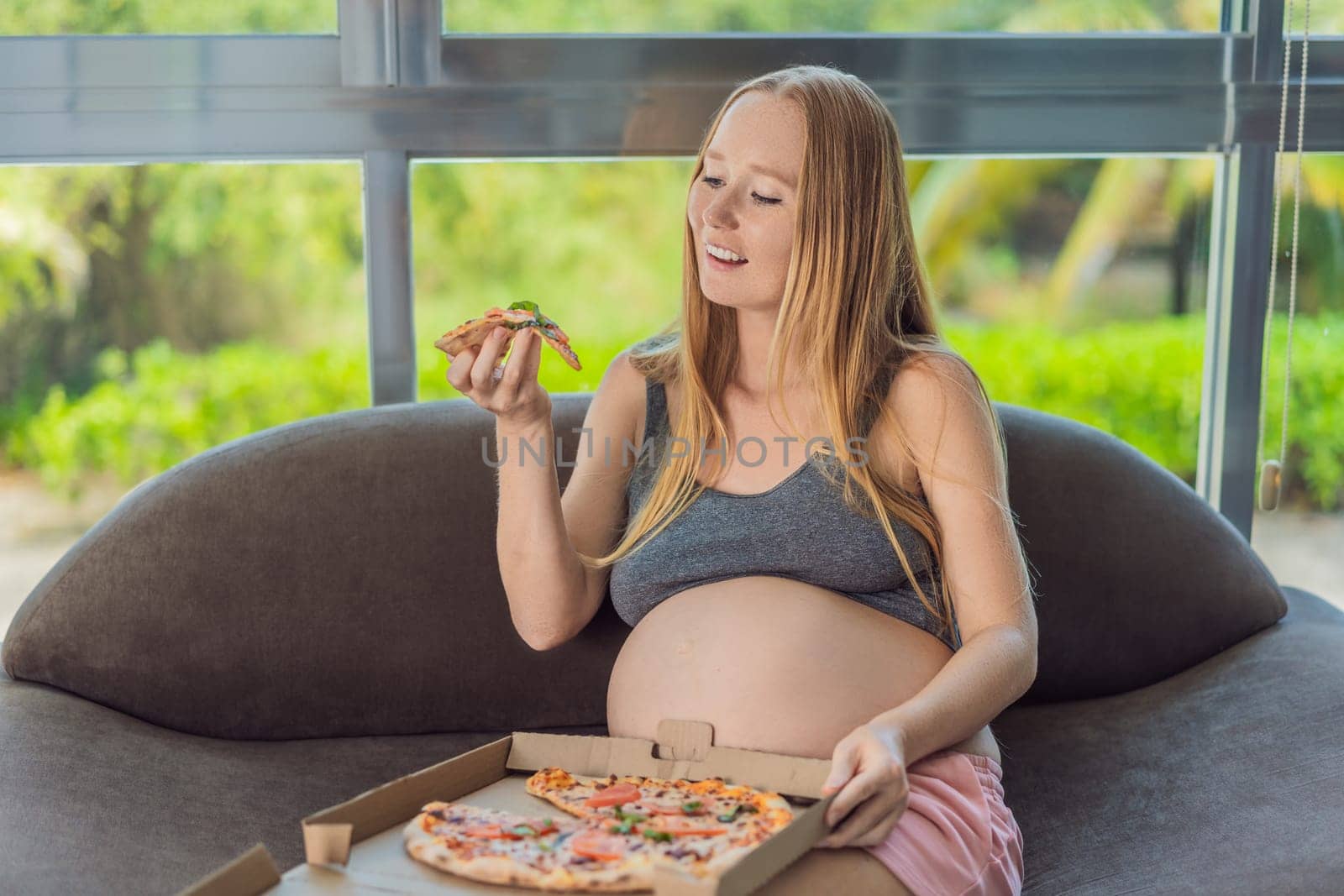 A pregnant woman enjoys a slice of pizza, savoring a moment of indulgence while satisfying her craving for a delightful, comforting treat. Excited Pregnant Young Lady Enjoying Pizza Holding Biting Tasty Slice Posing With Carton Box. Junk Food Lover Eating Italian Pizza. Unhealthy Nutrition Cheat Meal by galitskaya