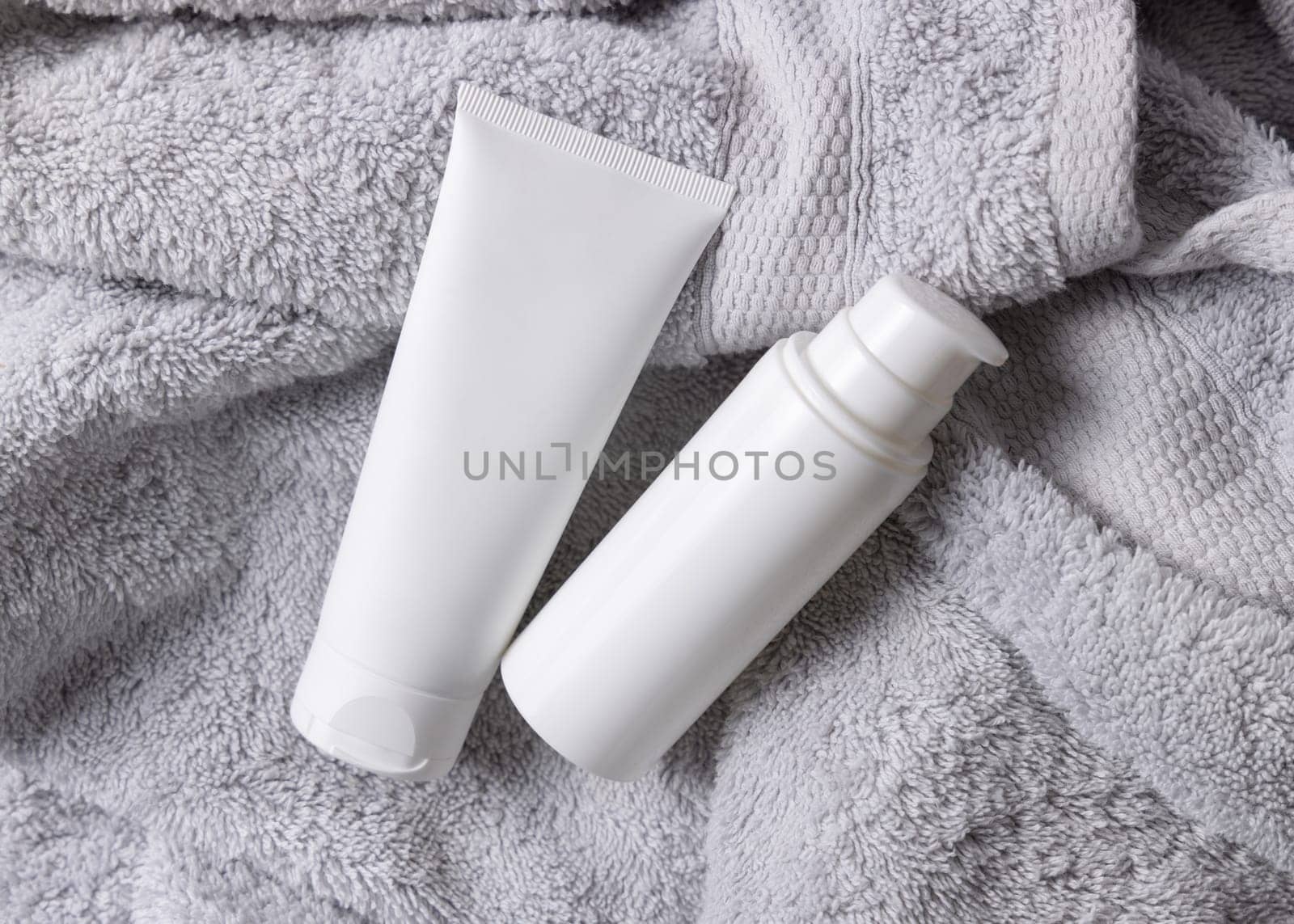 White blank cosmetic squeeze cream tube one pump bottle on light gray towel in bathroom top view, brand packaging mockup. Natural herbal cosmetic product for daily facecare, copy space