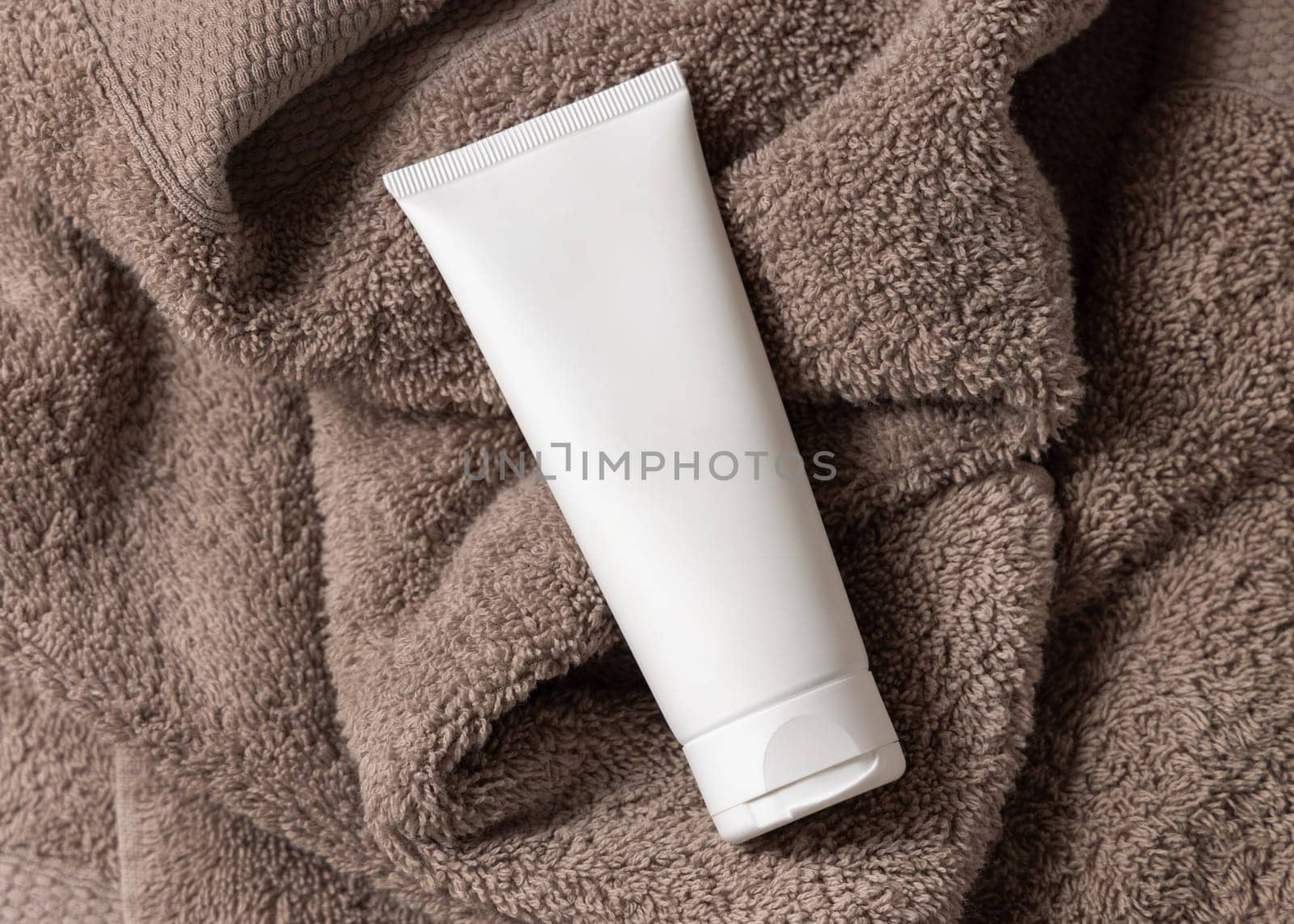White blank squeeze cream tube on brown towel in bathroom top view, brand packaging mockup, copy space. Natural handmade cosmetic product for facecare and spa procedures
