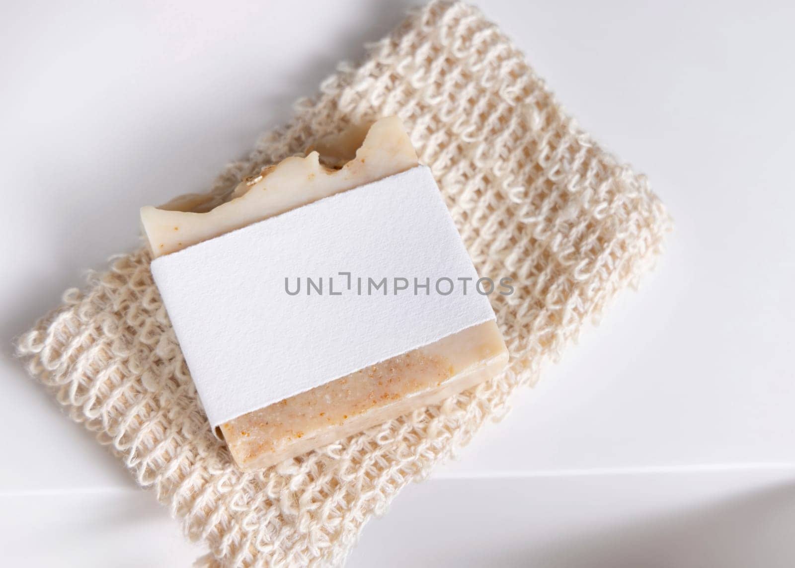 Beige handmade soap bar with blank label on sisal soap saver bag on washbasin close up, packaging mockup, copy space. Natural herbal unbranded product for daily hygiene