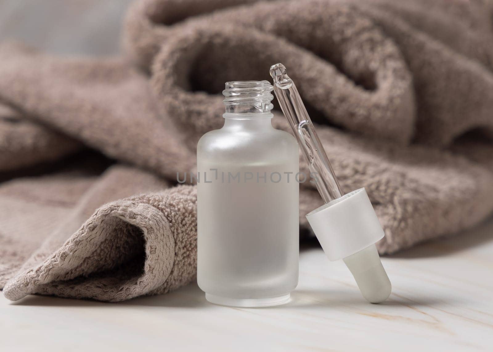 Pipette set near an opened clear glass glass dropper bottle filled with liquid near light brown bath towel close up, mockup. Natural serum or essence for daily beauty facecare
