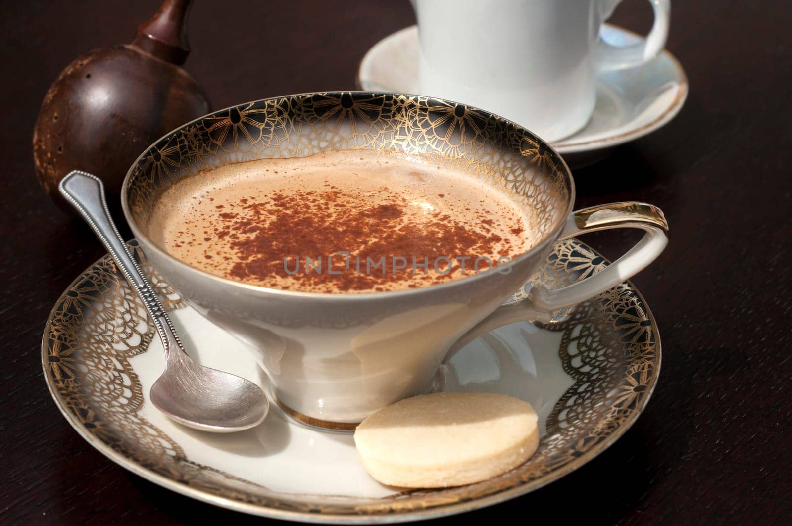 Fine porcelain cup with coffee, milk and sprinkled cinnamon on dark background