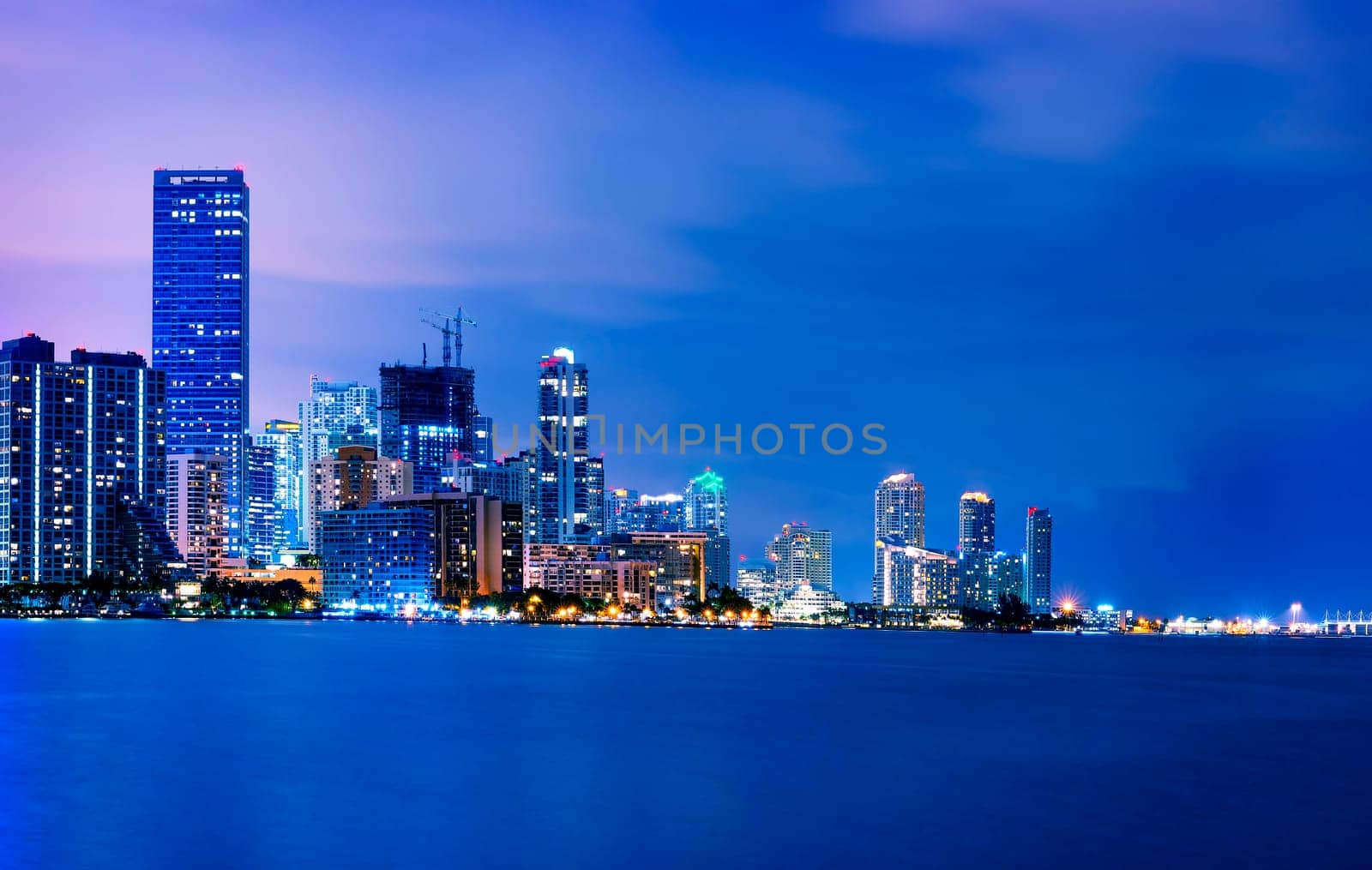 Miami city skyline panorama at dusk with urban skyscrapers over sea with reflection