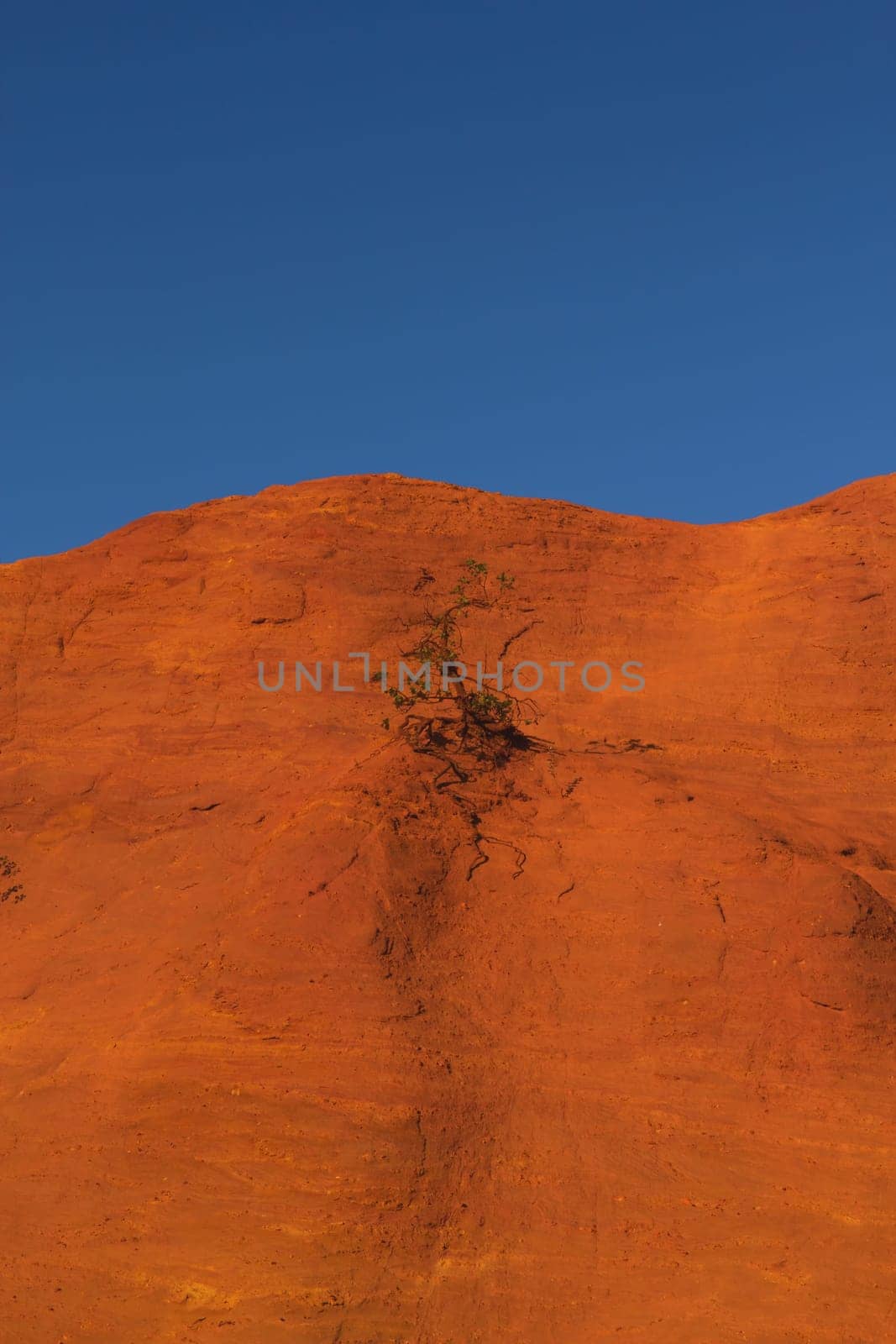 Red and orange ocher hill with blue sky in the background. 2/3 hill and 1/3 blue sky. Le Colorado Provencal de Rustrel (France). Vertically.