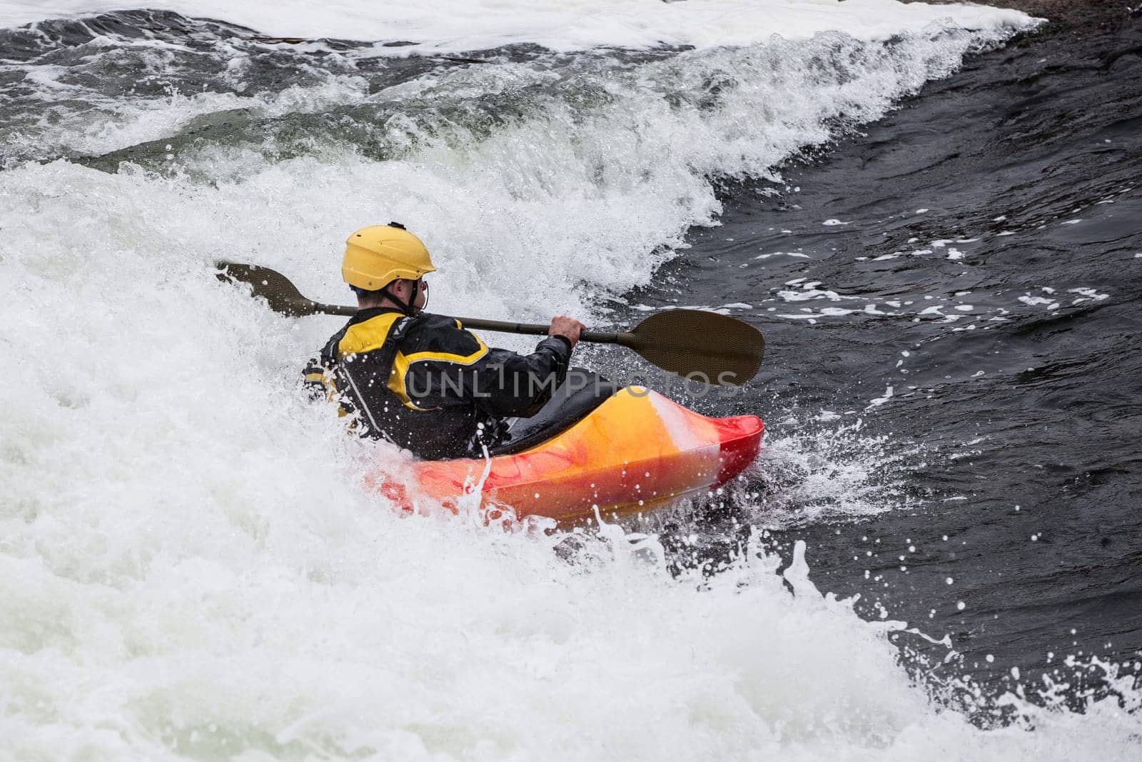 an active male kayaker rolling and surfing in rough water