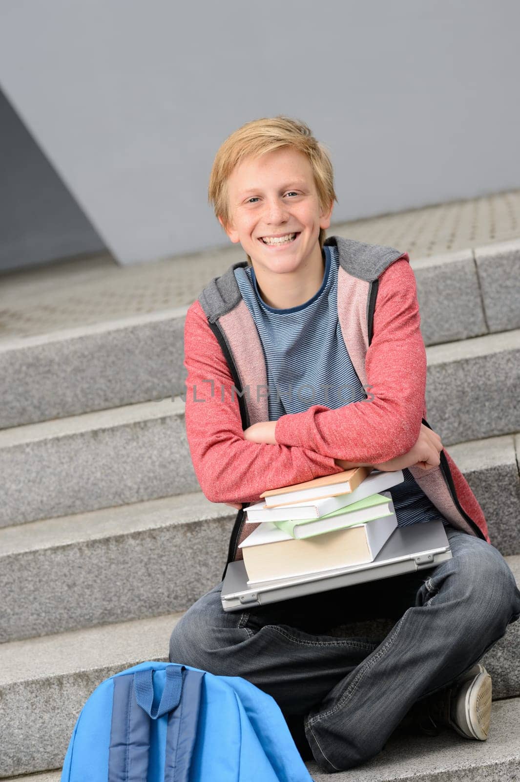 Happy student with books and laptop sitting outside on steps