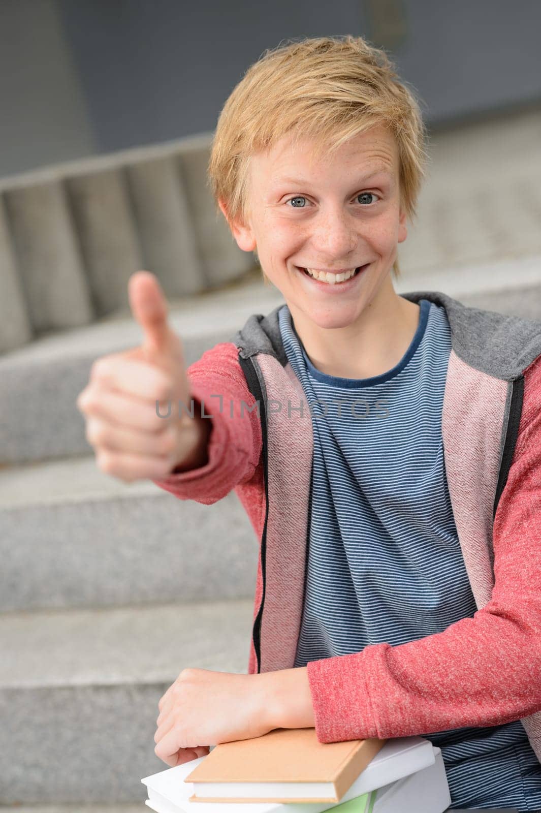 Successful student with books show thumb-up sitting outside on steps