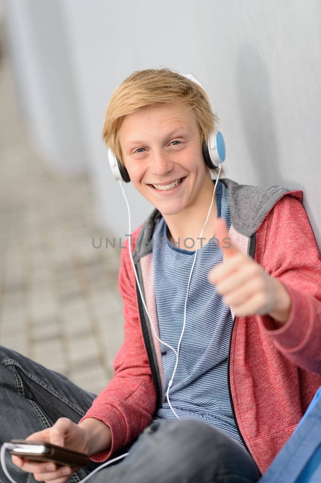 Successful teenage student thumb-up listening to music sitting outside