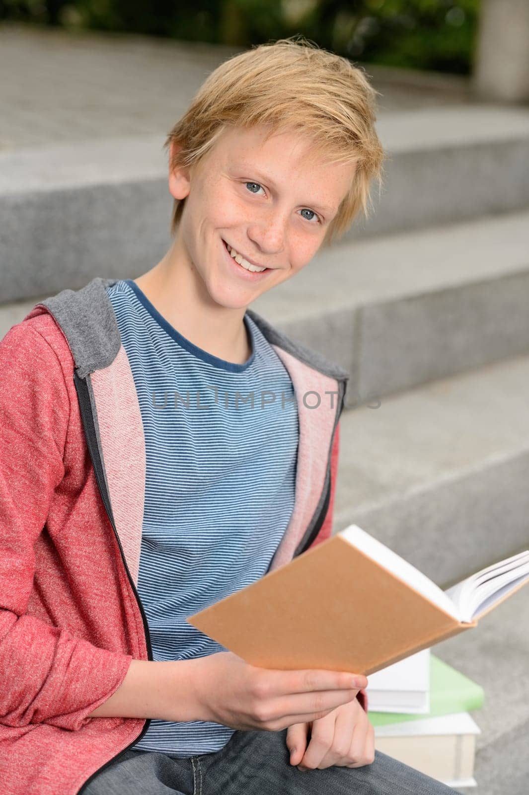 Happy teenage boy studying while sitting on school steps