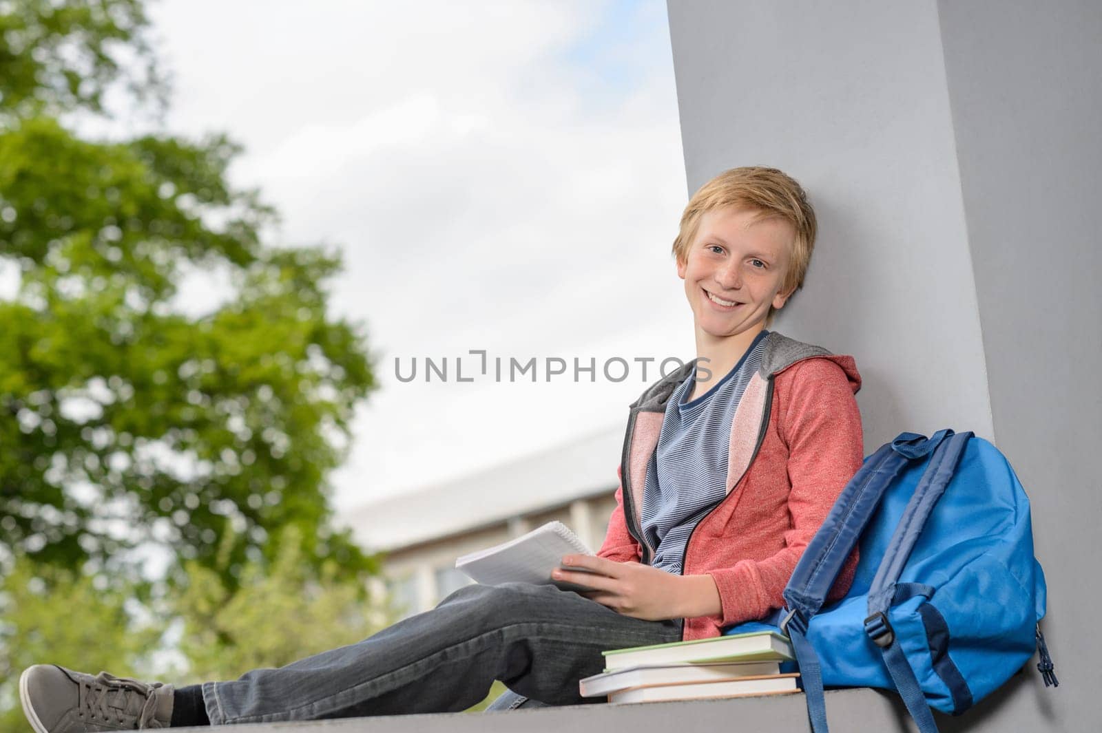 Happy teenage boy studying on wall outside his school campus
