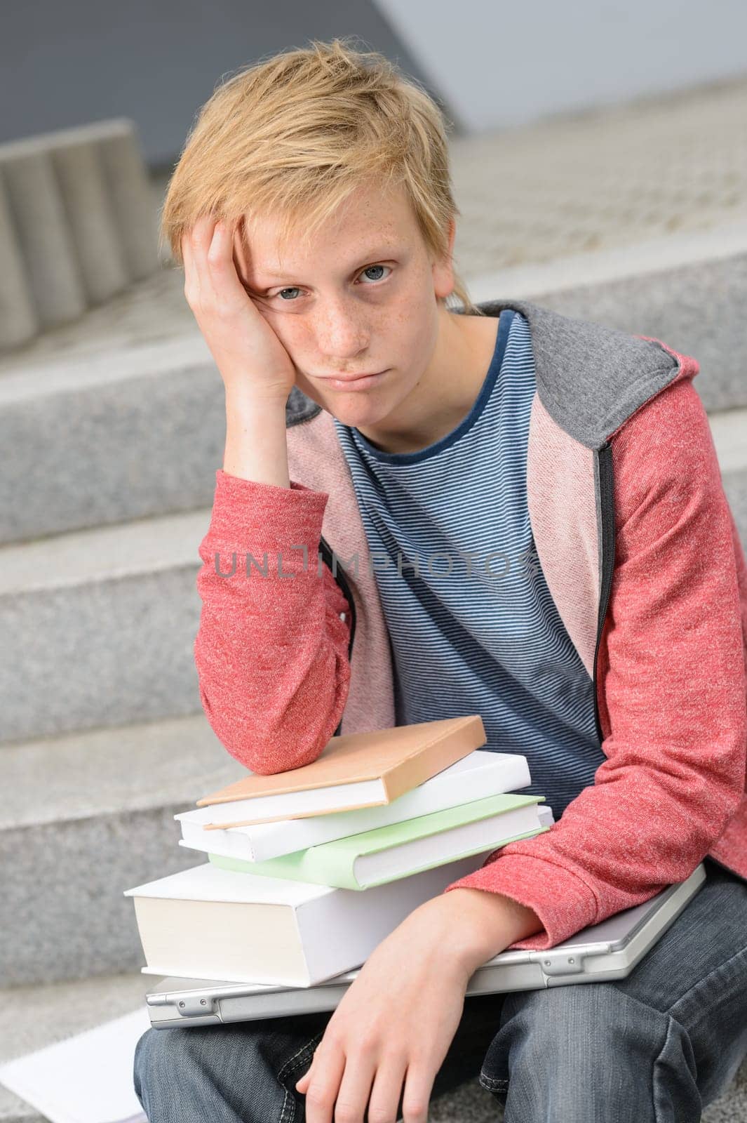 Bored student with books and laptop sitting outside on steps
