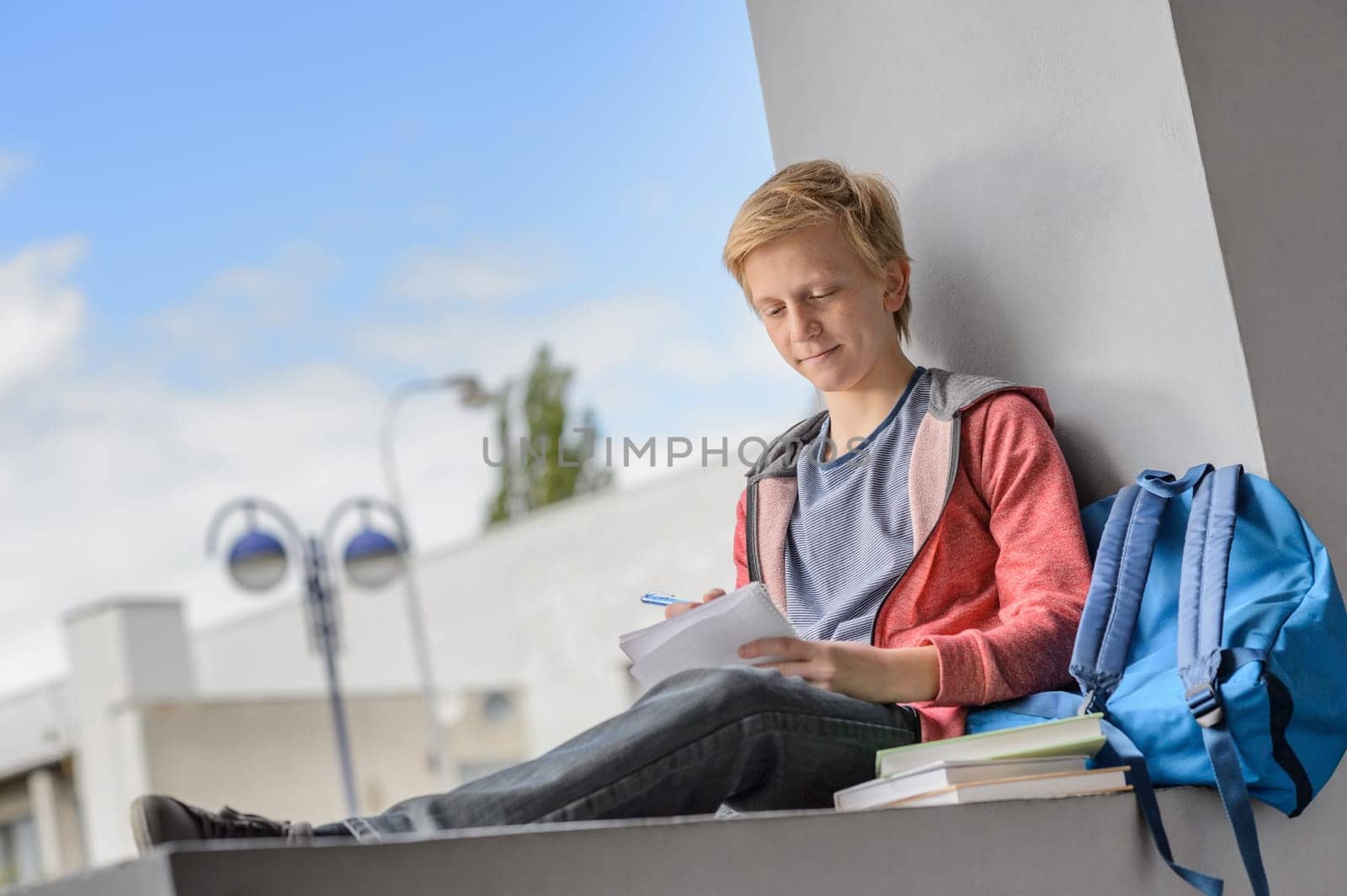 Teenage boy studying while sitting on wall at university campus